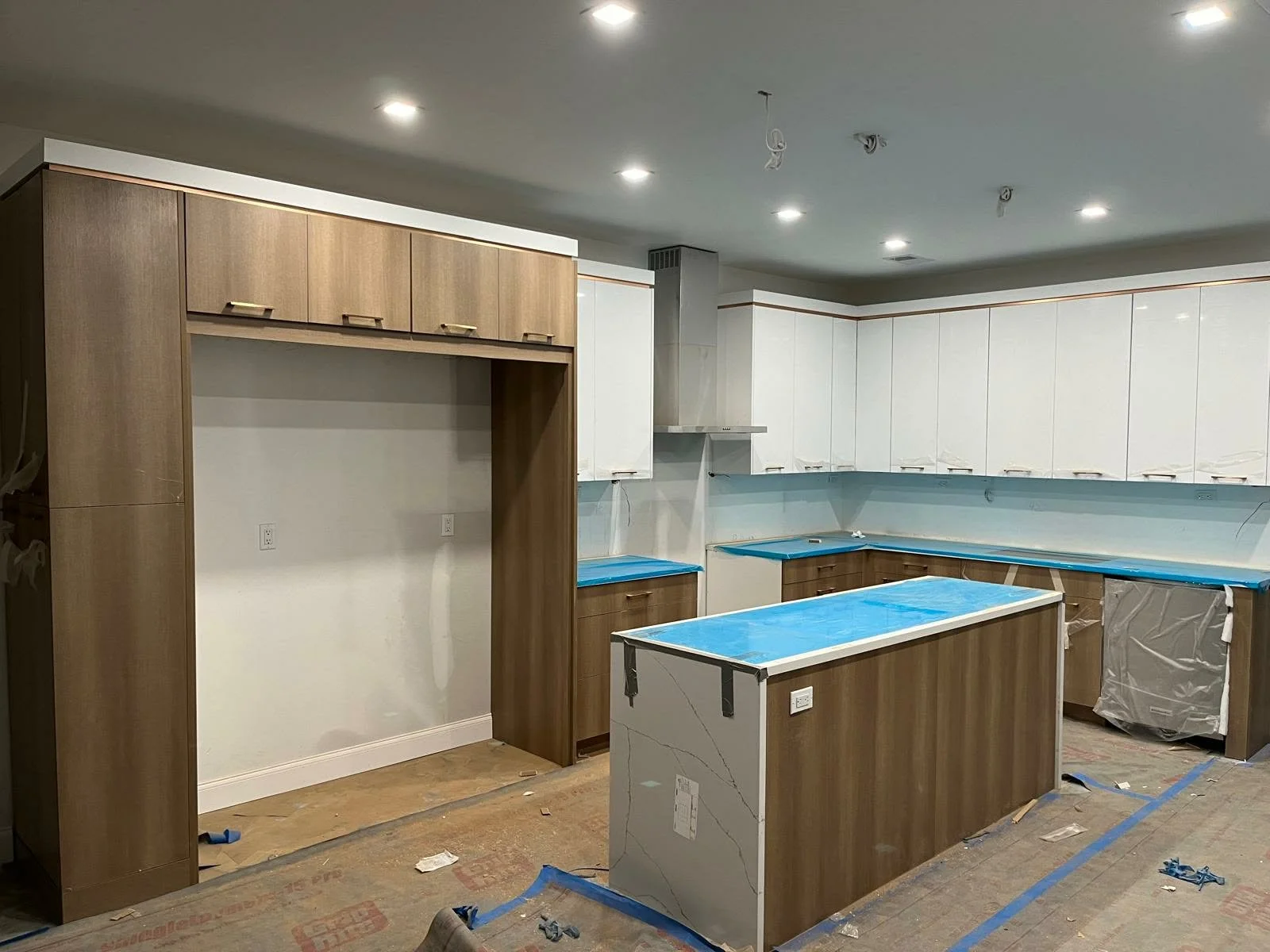 Kitchen under renovation with wood and white cabinets, blue painter's tape, and construction debris on the floor.