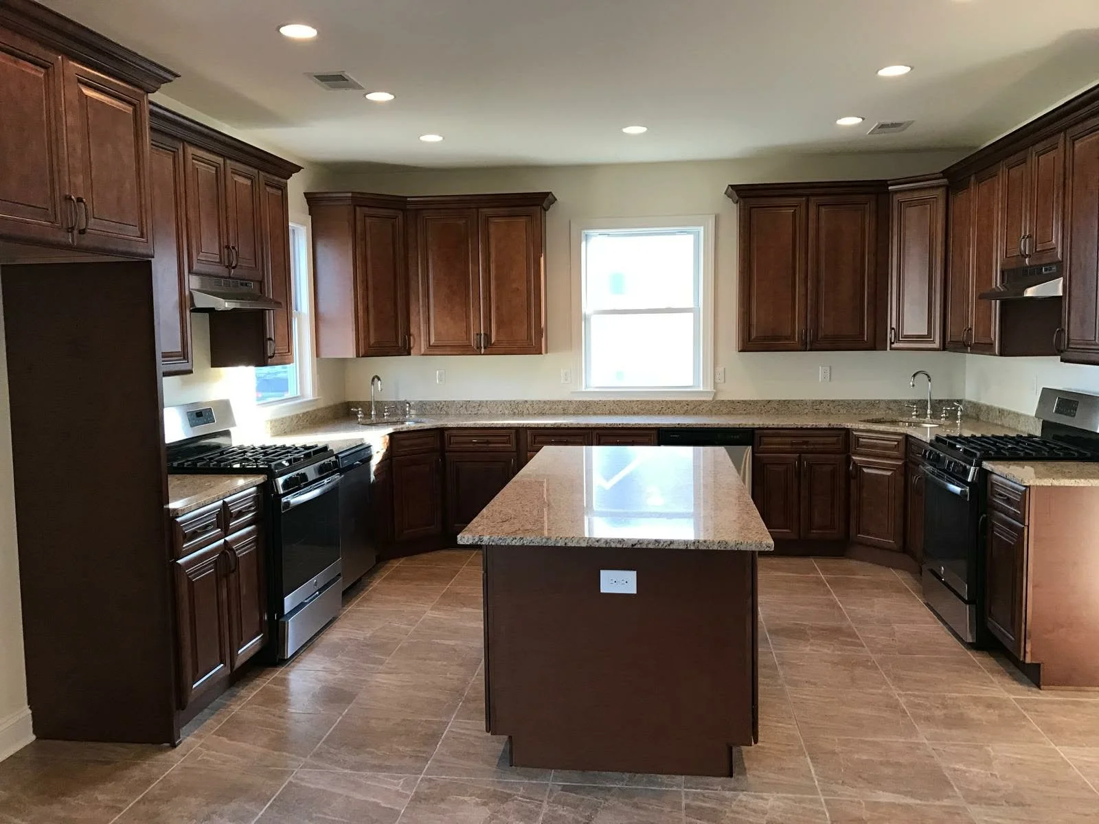 Modern kitchen with wooden cabinets, granite countertops, a central island, black appliances, and tiled flooring.