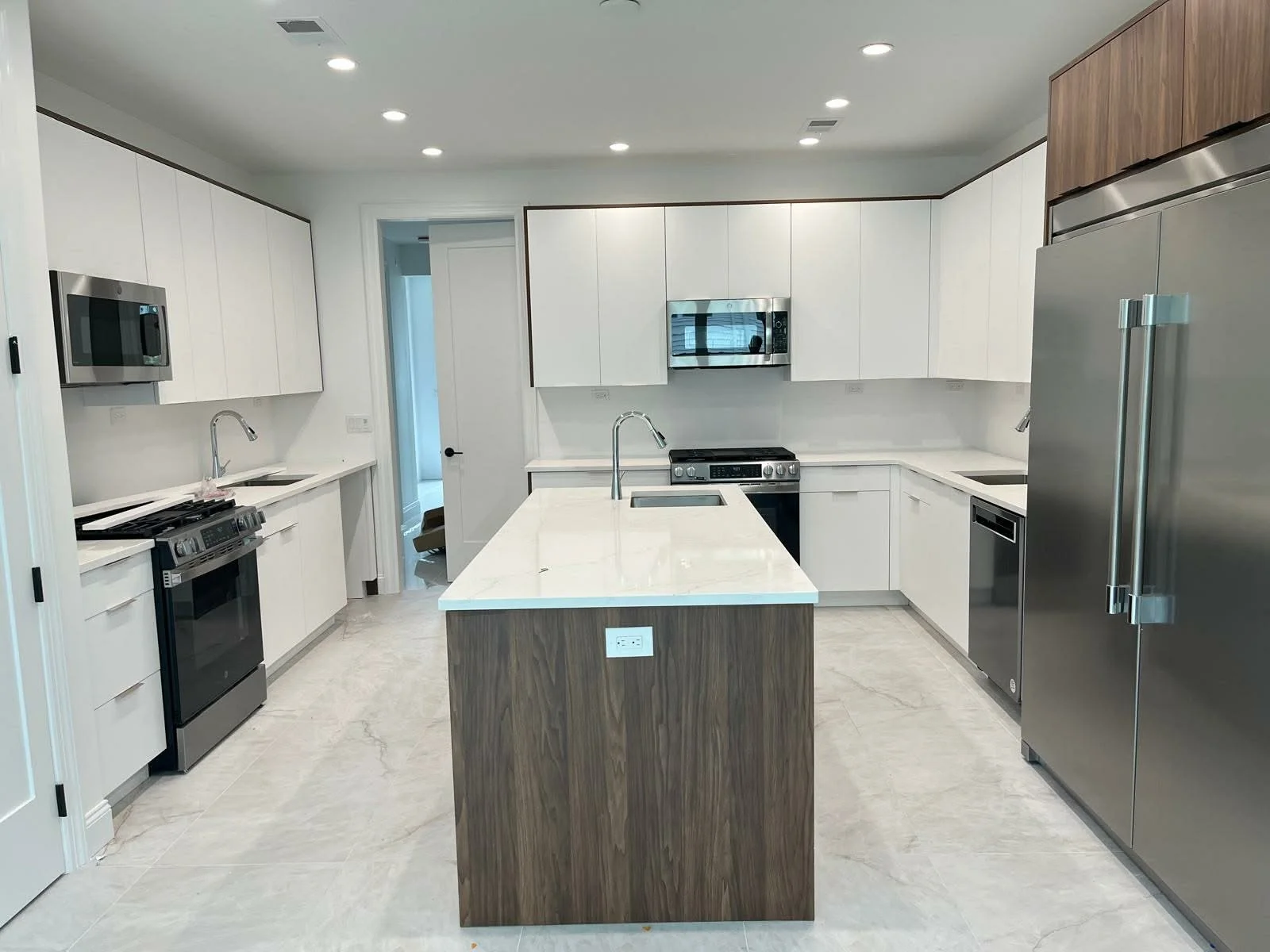 Modern kitchen with white cabinetry, stainless steel appliances including a refrigerator, microwave, stove, and dishwasher, and a central island with a marble countertop.