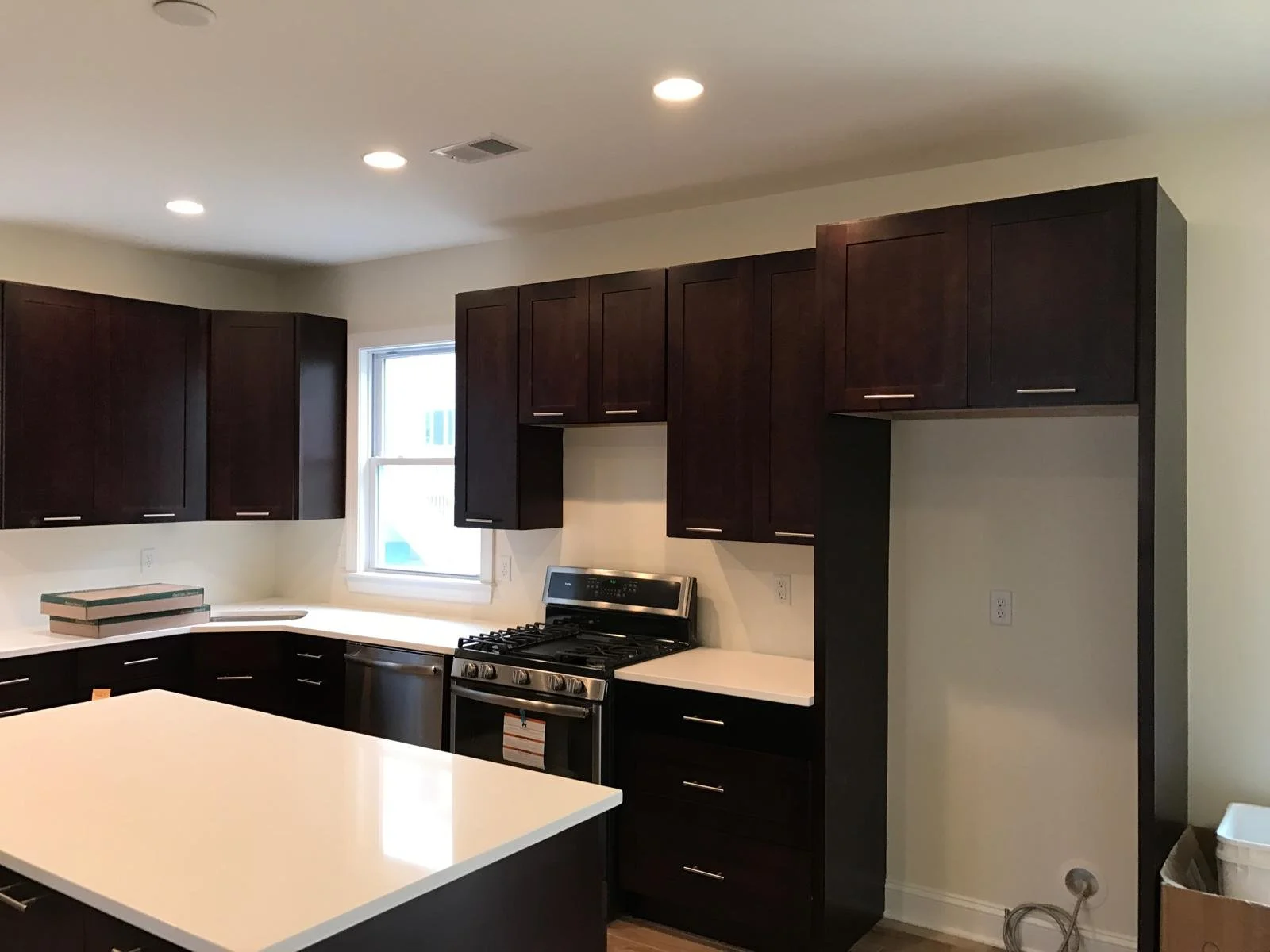 Kitchen with dark cabinets, white countertops, window, and stainless steel gas stove.
