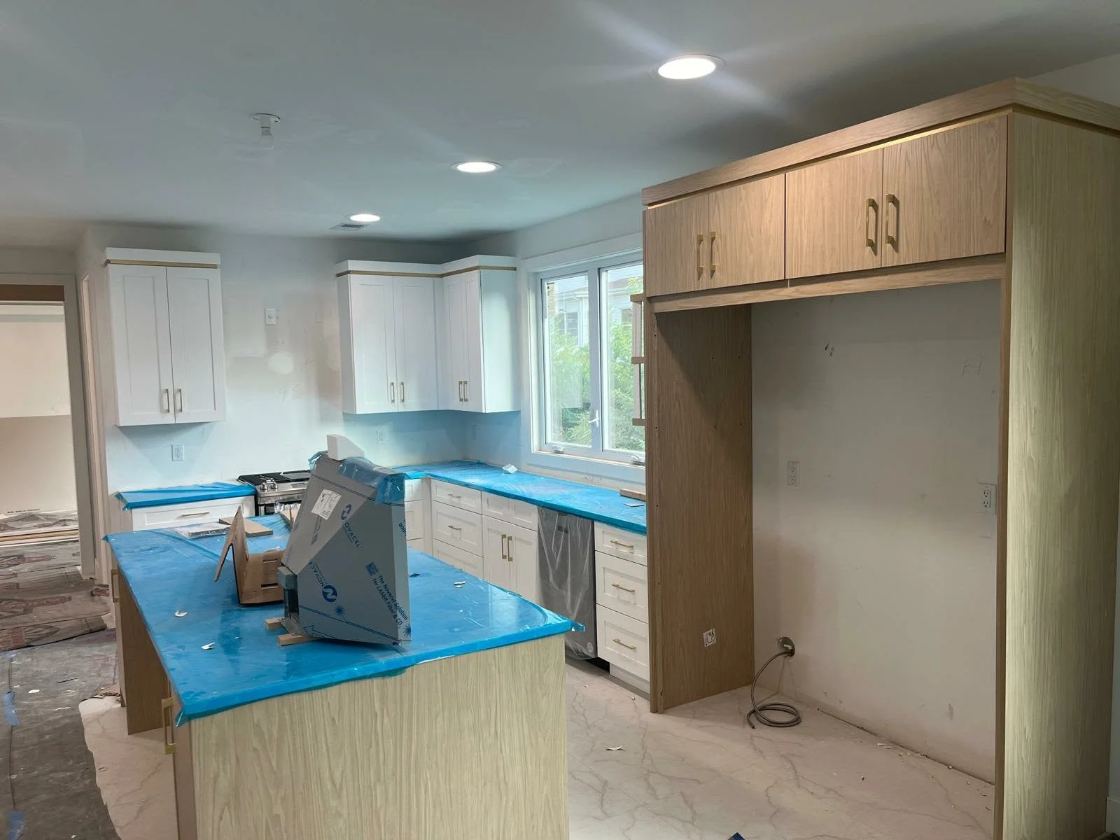 Kitchen in the process of renovation with white cabinets, a central island covered with blue protective plastic, and unfinished wooden structures.