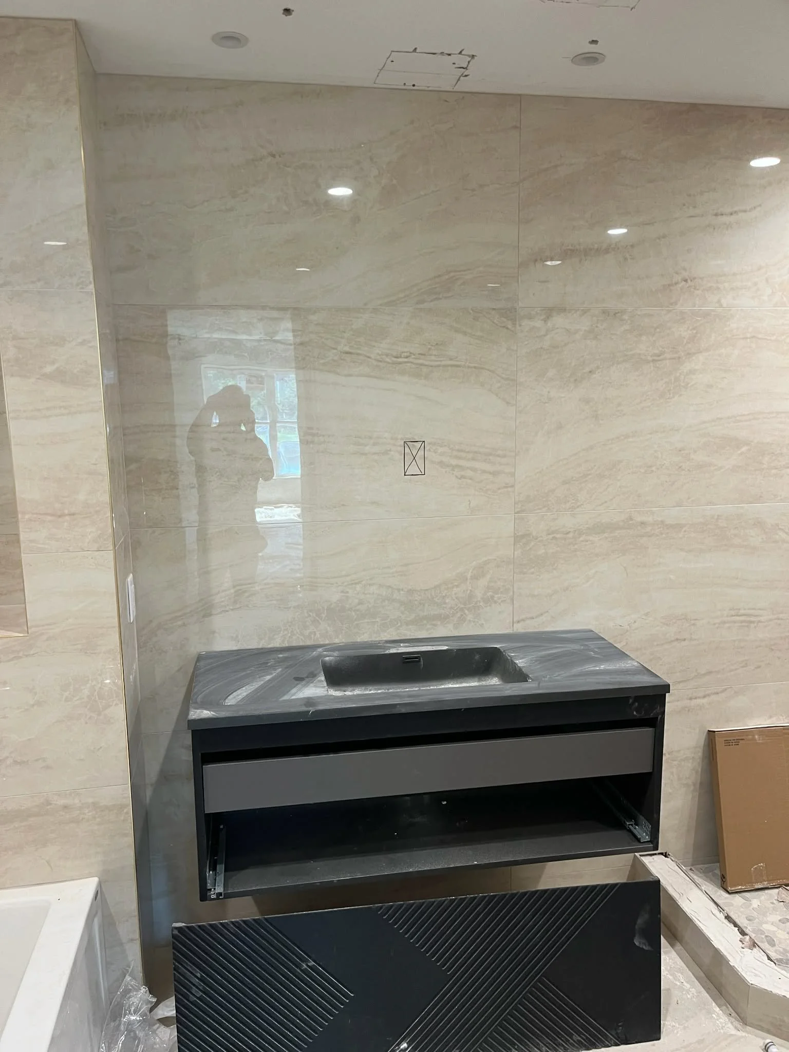 Empty black display case with glass top in a store or showroom, with beige marble wall behind and some packaging materials and an art piece on the floor