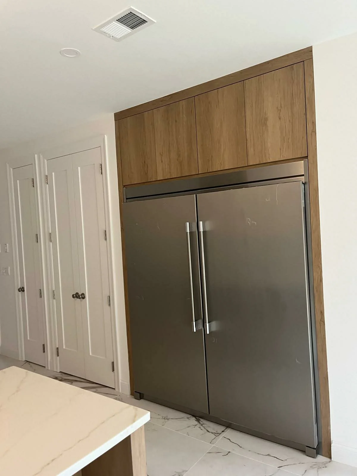 Modern kitchen with stainless steel double refrigerator, white cabinets, and marble flooring.