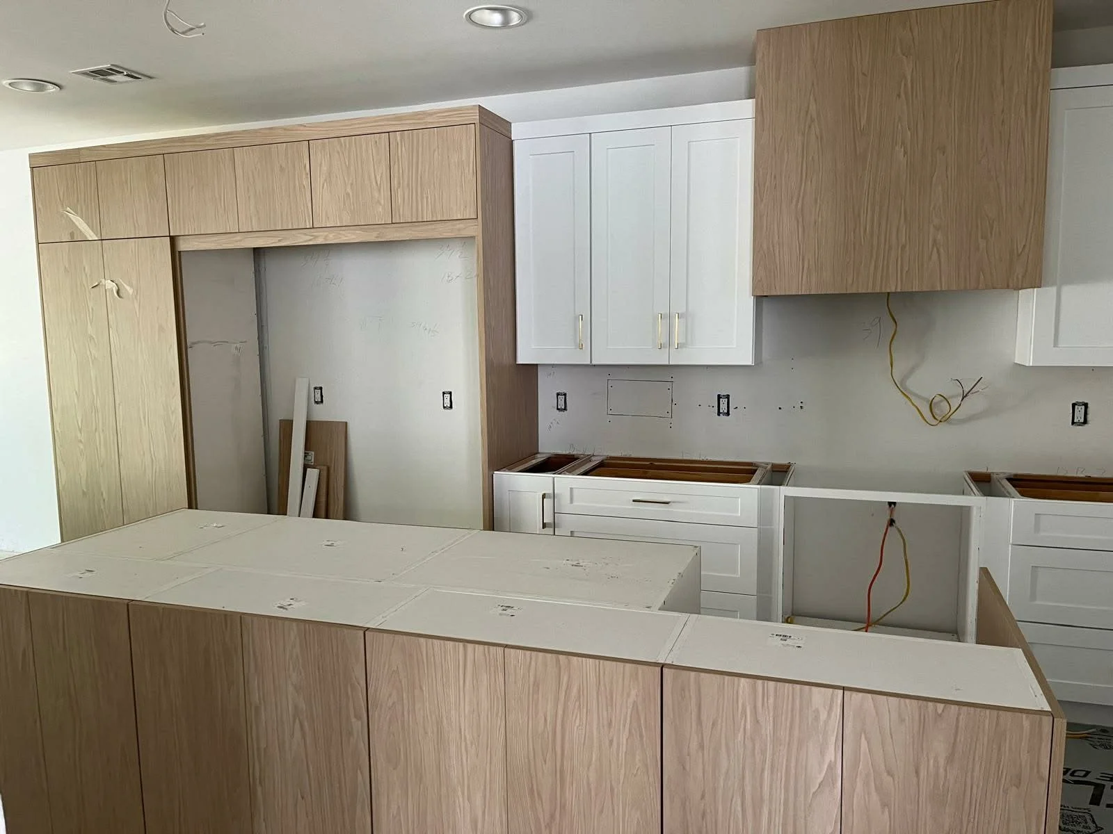 Kitchen under construction with unfinished cabinets and wiring exposed.