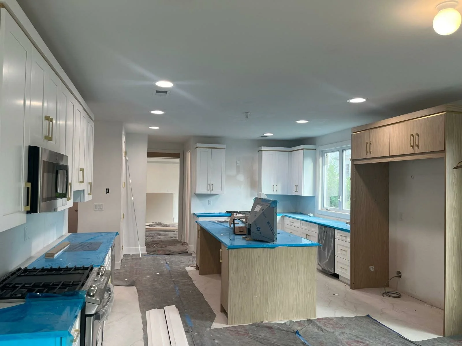 Kitchen under construction with white cabinetry, a central island, and blue protective coverings on surfaces, during renovation.