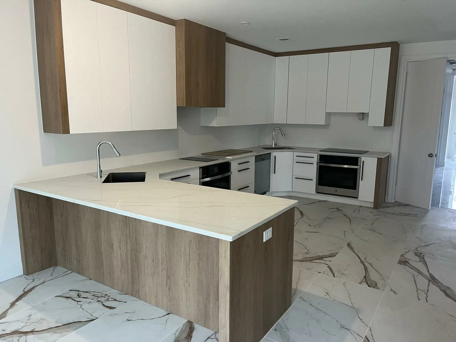 Modern kitchen with white and wood cabinetry, marble counter island, marble flooring, and stainless steel appliances.