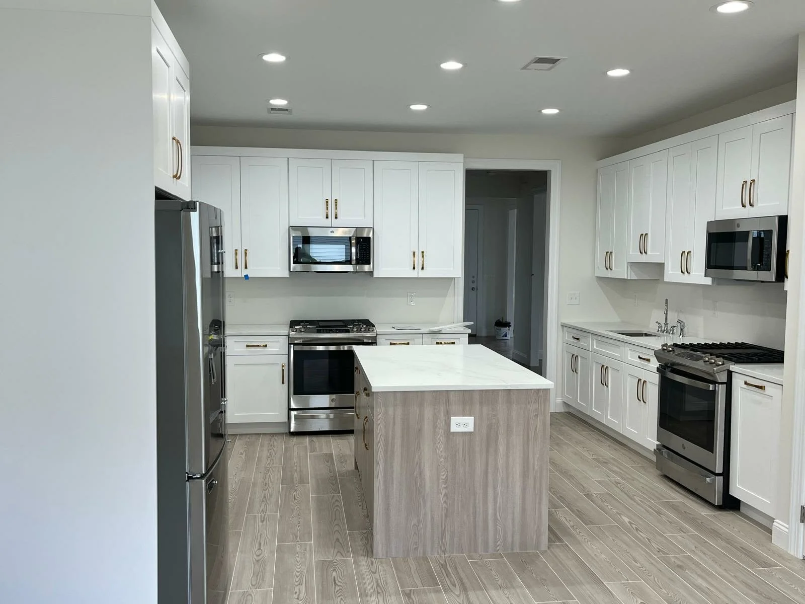 Modern kitchen with white cabinets, stainless steel appliances including a fridge, microwave, and stove, a kitchen island with a light wood finish, and recessed lighting on the ceiling.