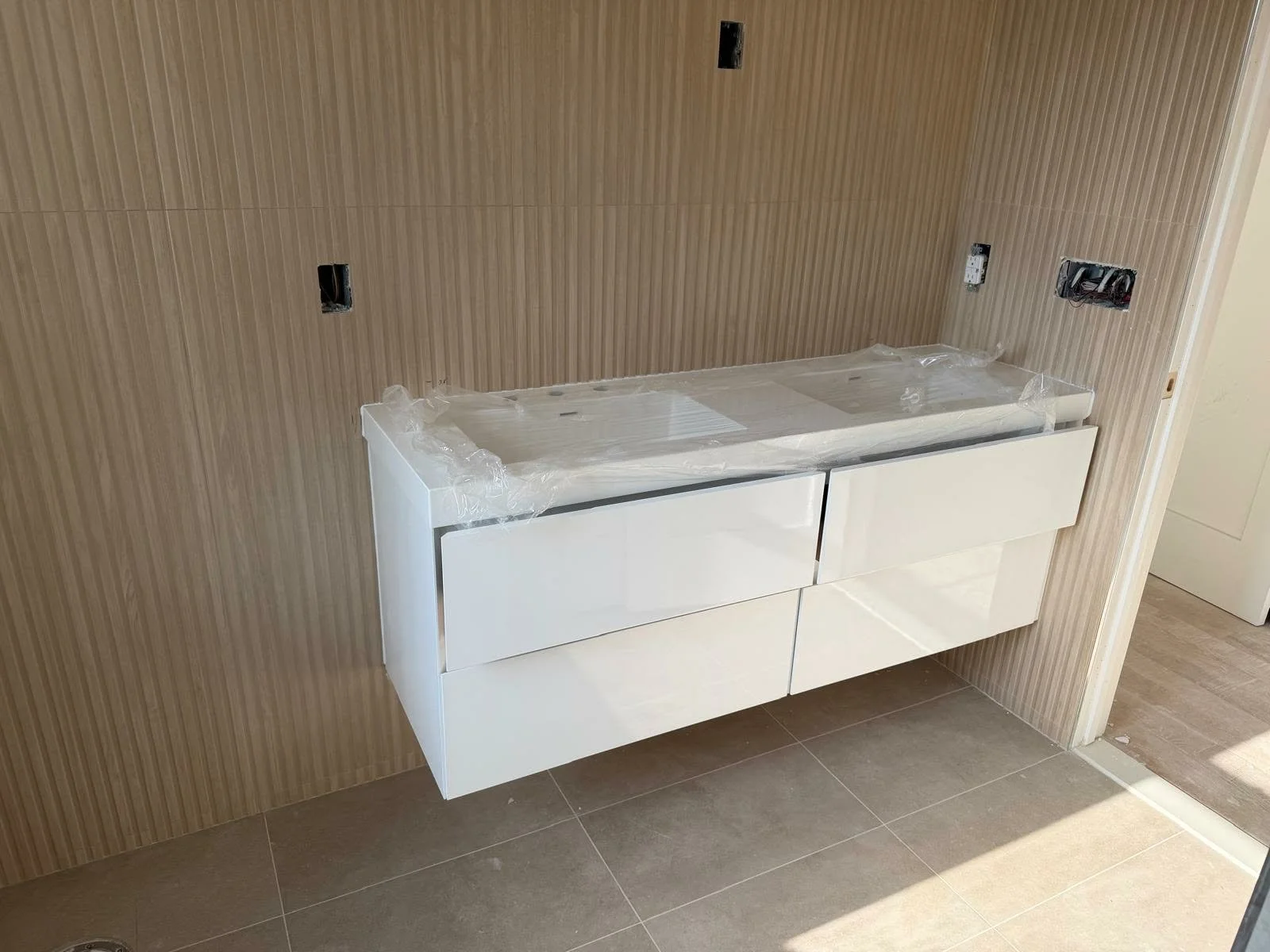 Bathroom vanity with drawers mounted on a wall, with wiring and electrical outlets visible above, in a room under construction or renovation.