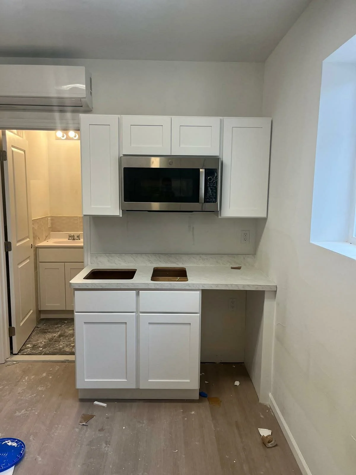 Kitchen with white cabinets, a microwave oven, and a marble countertop, with a doorway leading to a small bathroom in the background.