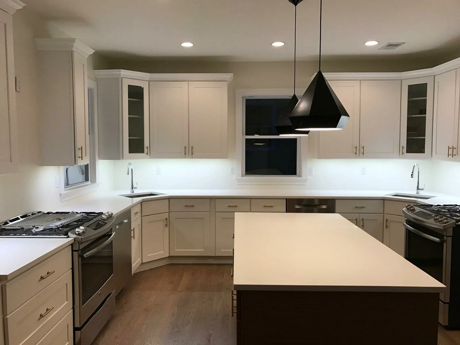 A modern kitchen with white cabinets, a central island, stainless steel appliances, and two black pendant lights hanging from the ceiling.