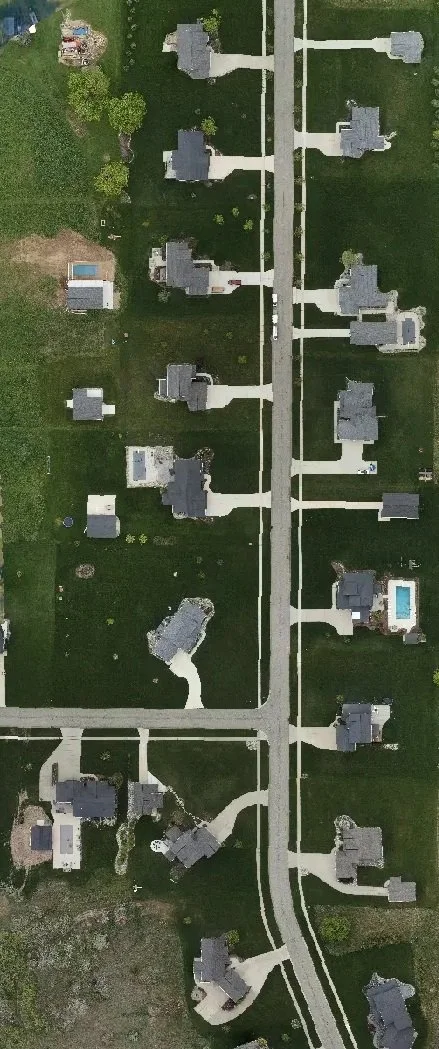 Aerial view of a suburban neighborhood with houses, driveways, and yards, including a few with swimming pools.