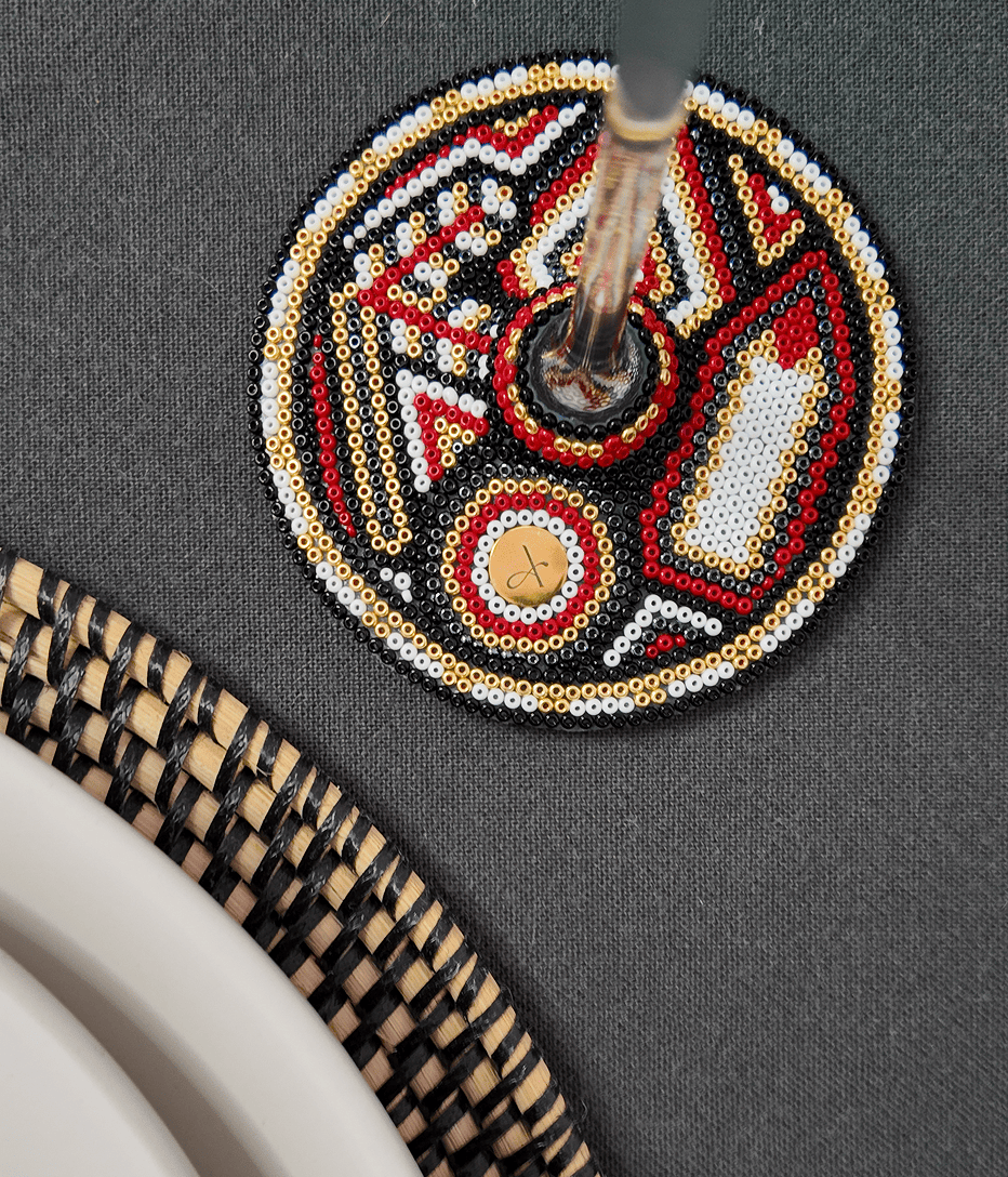 Detalle de la base de una copa decorada con arte huichol / wixárica, en una mesa elegante con mantel y plato artesanal