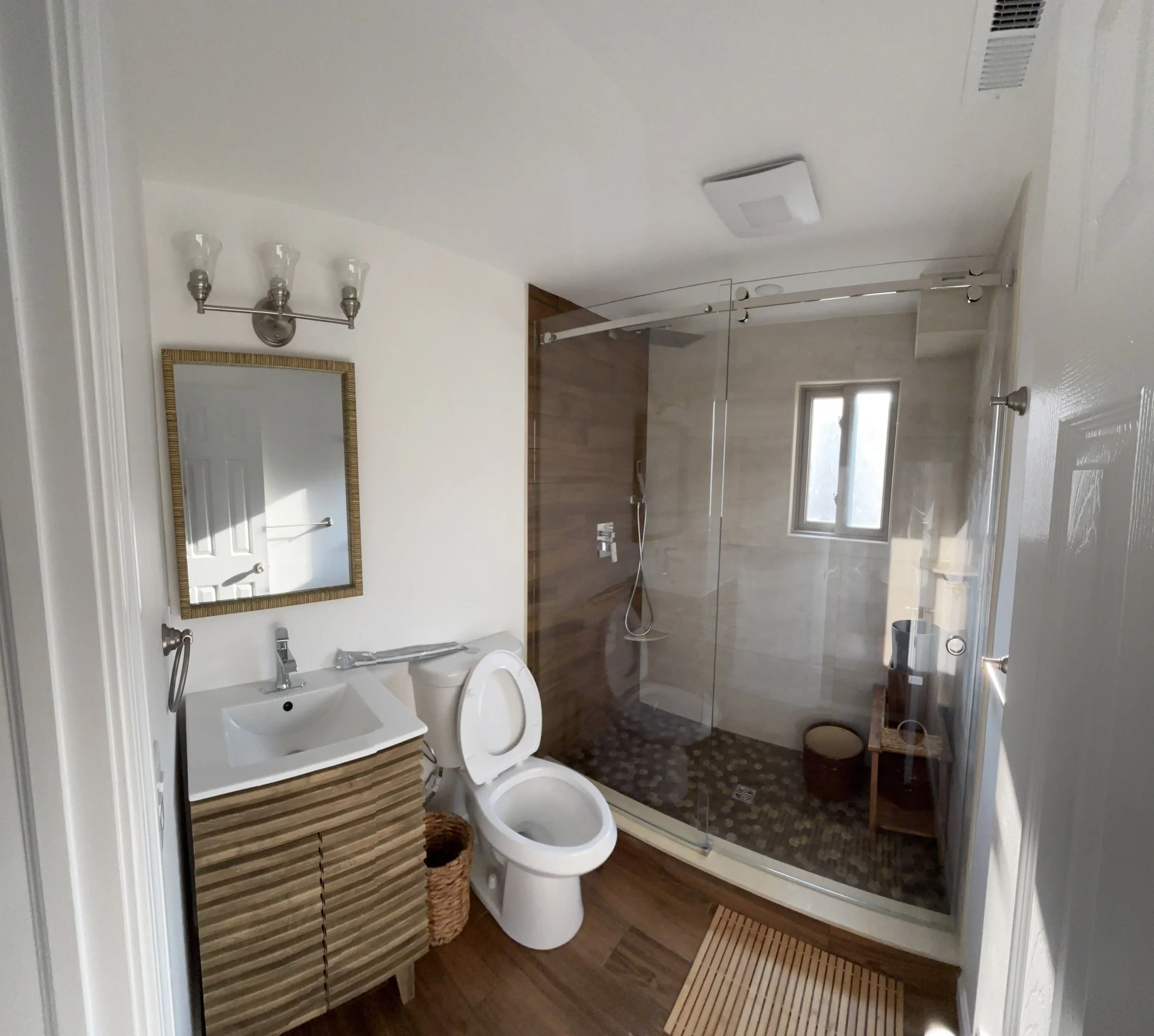 Completed bathroom renovation with modern tile shower, glass enclosure, vanity, and flooring.