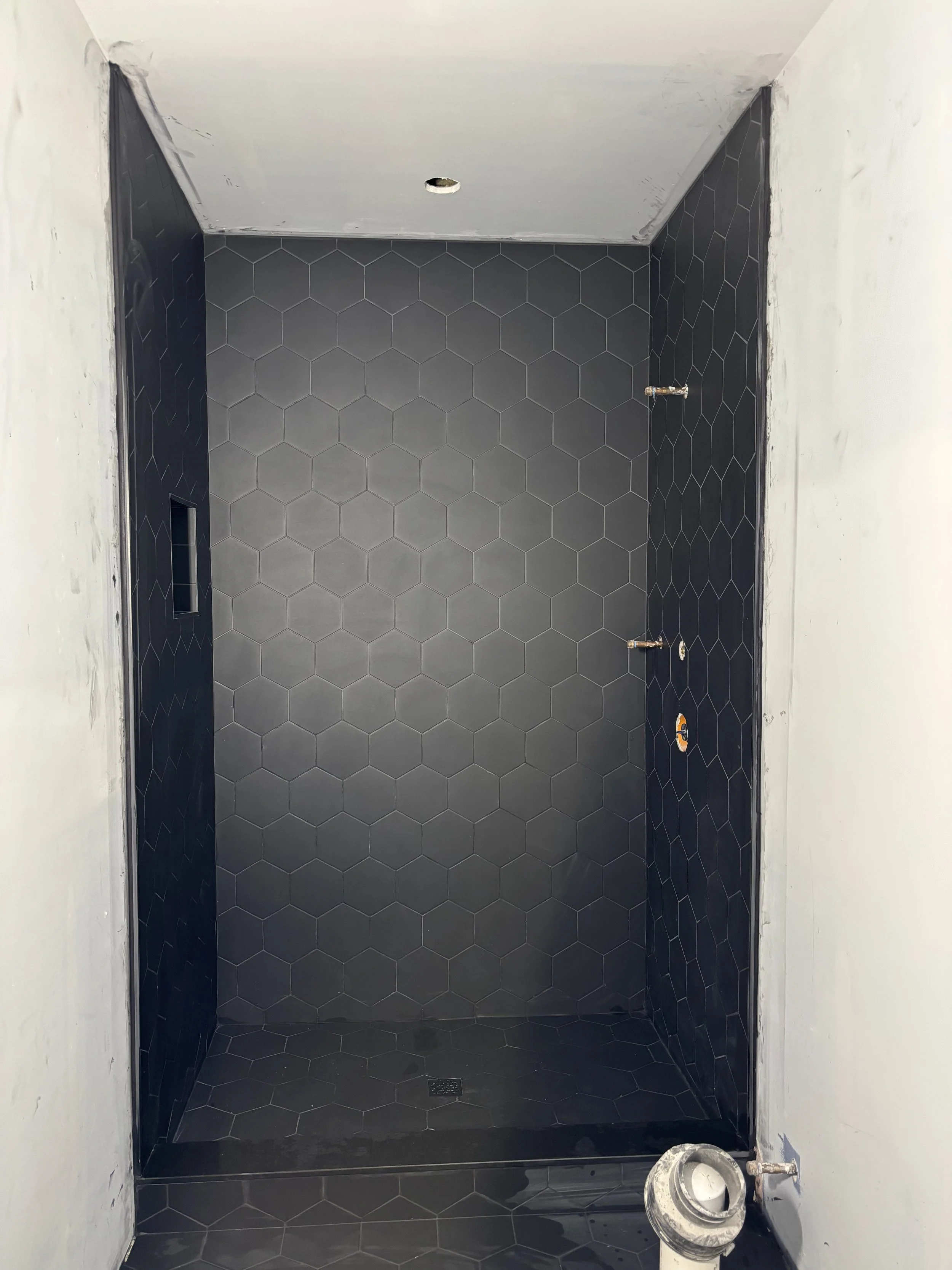 Custom shower installation in progress featuring black hexagon tile and detailed tile work