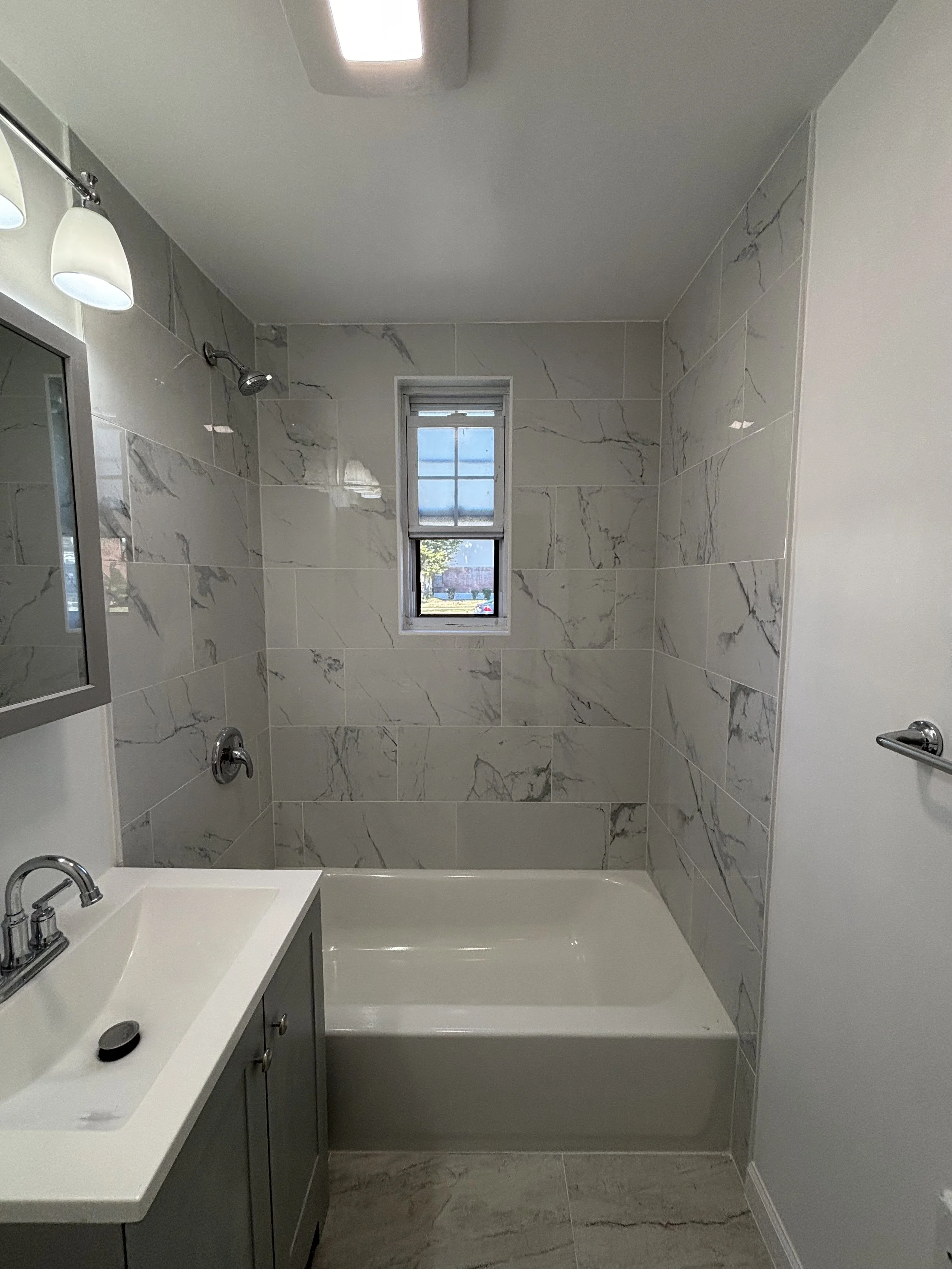 Renovation bathroom with marble-look tile, bathtub, vanity, mirror, and modern lighting.