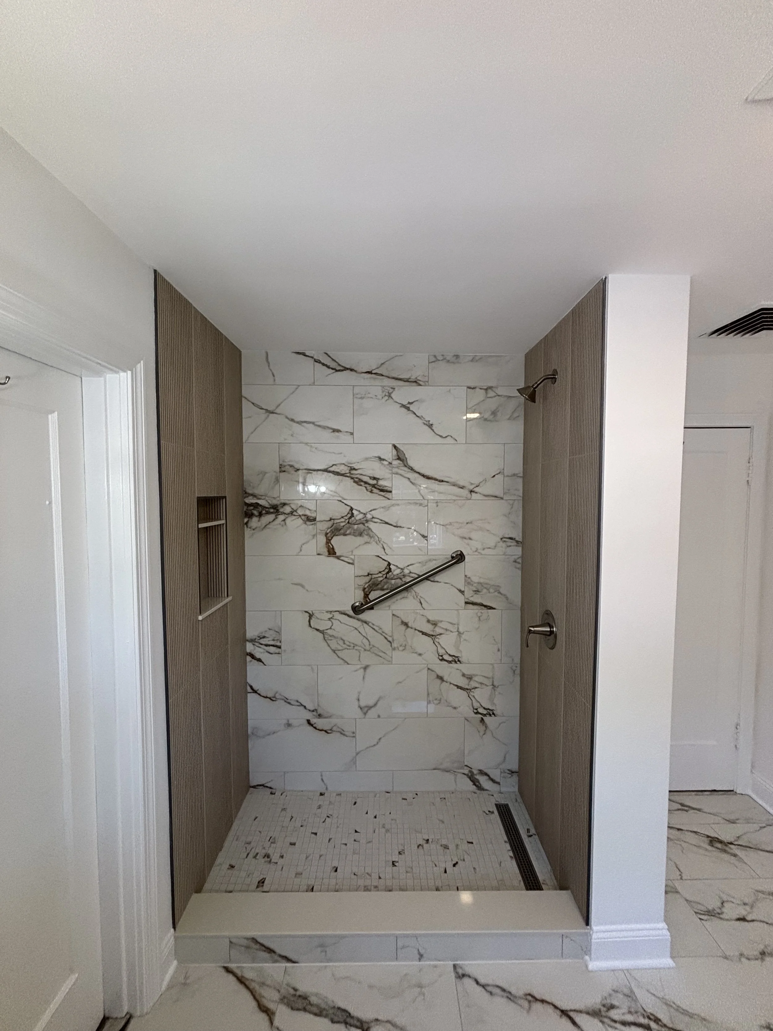 Custom marble-look tile shower with dual shower fixtures and grab bar.