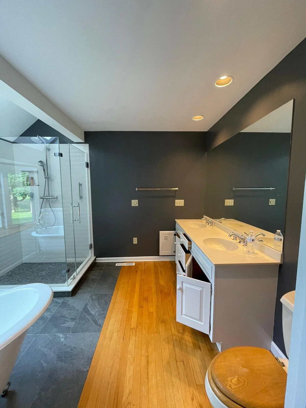 Renovated bathroom featuring tiled shower, dark shower floor, vanity, mirror, and wood-look flooring.