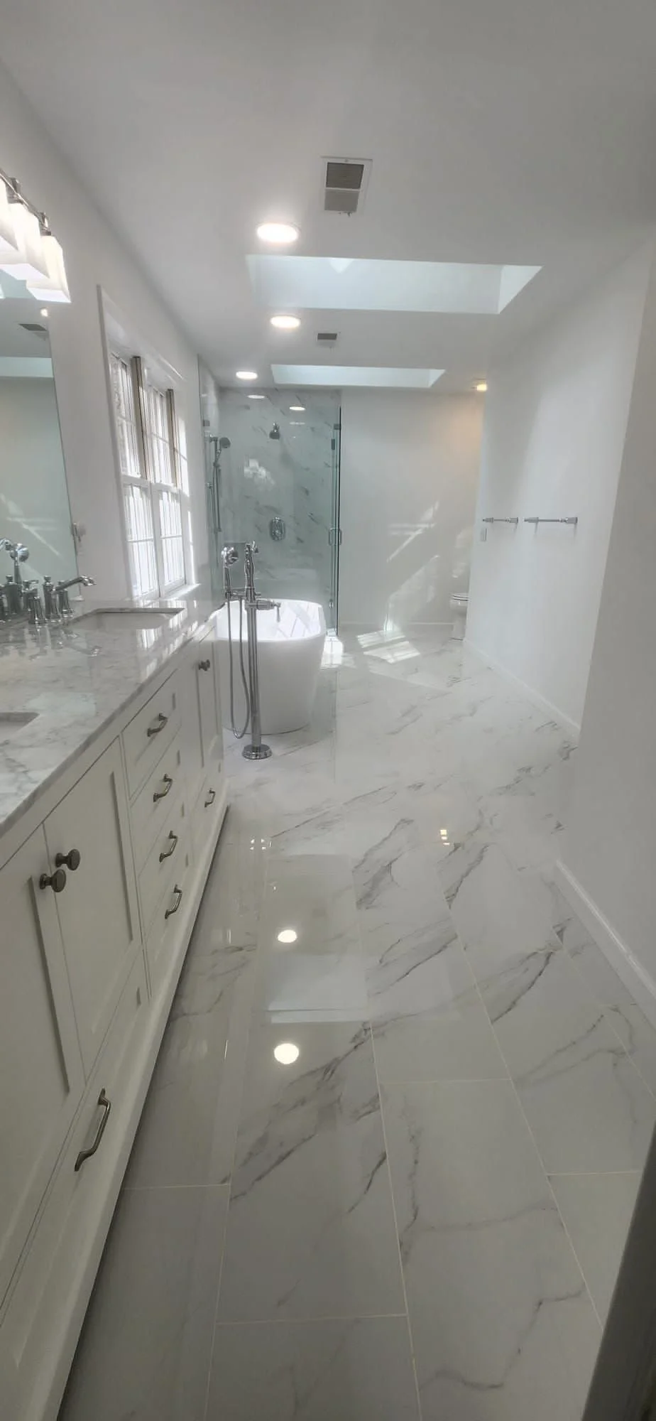 Modern bathroom renovation featuring marble tile, double vanity, bathtub, shower, and recessed lighting.