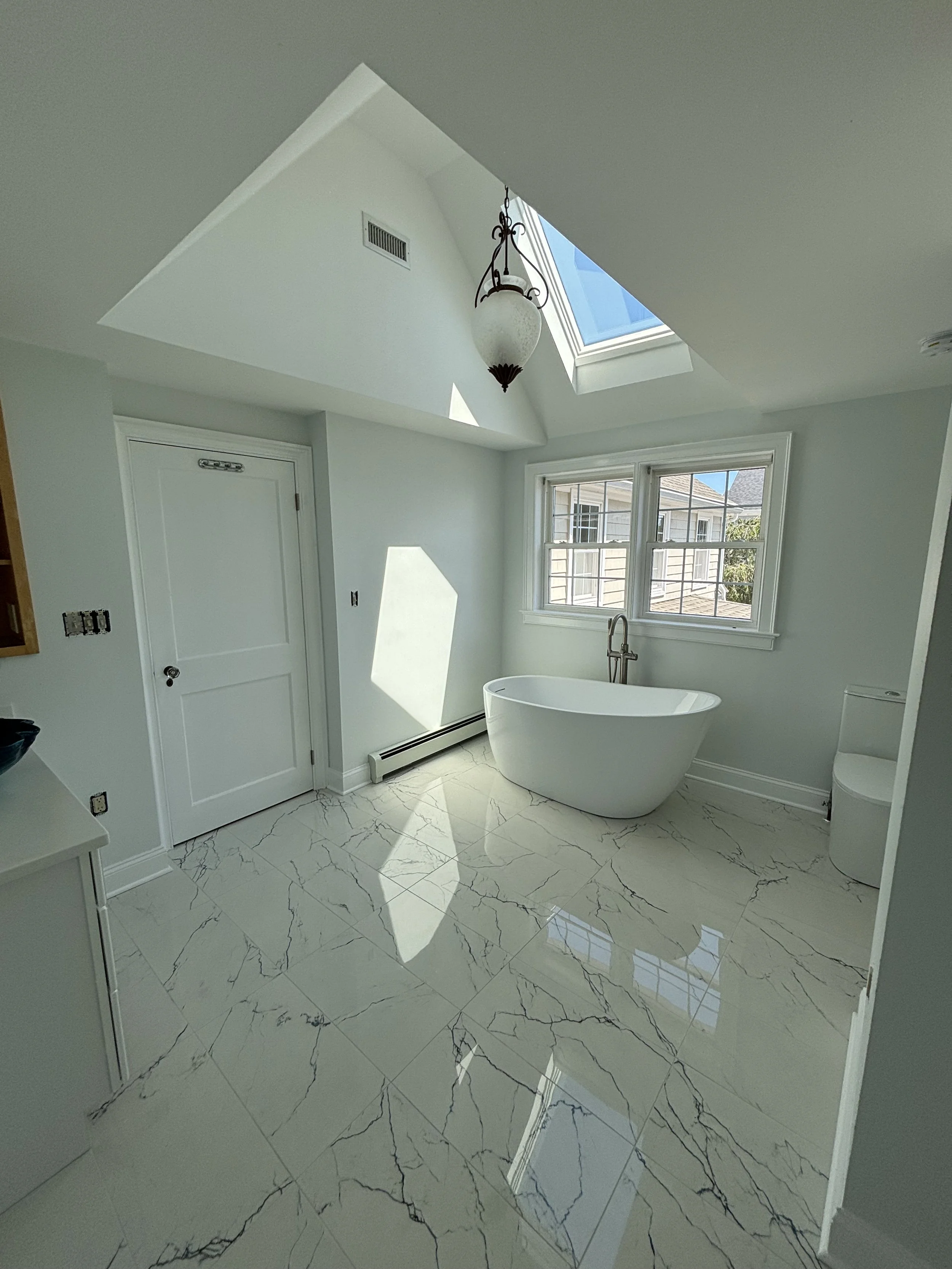 Bright bathroom renovation featuring freestanding tub, marble-look flooring, skylight, and modern finishes