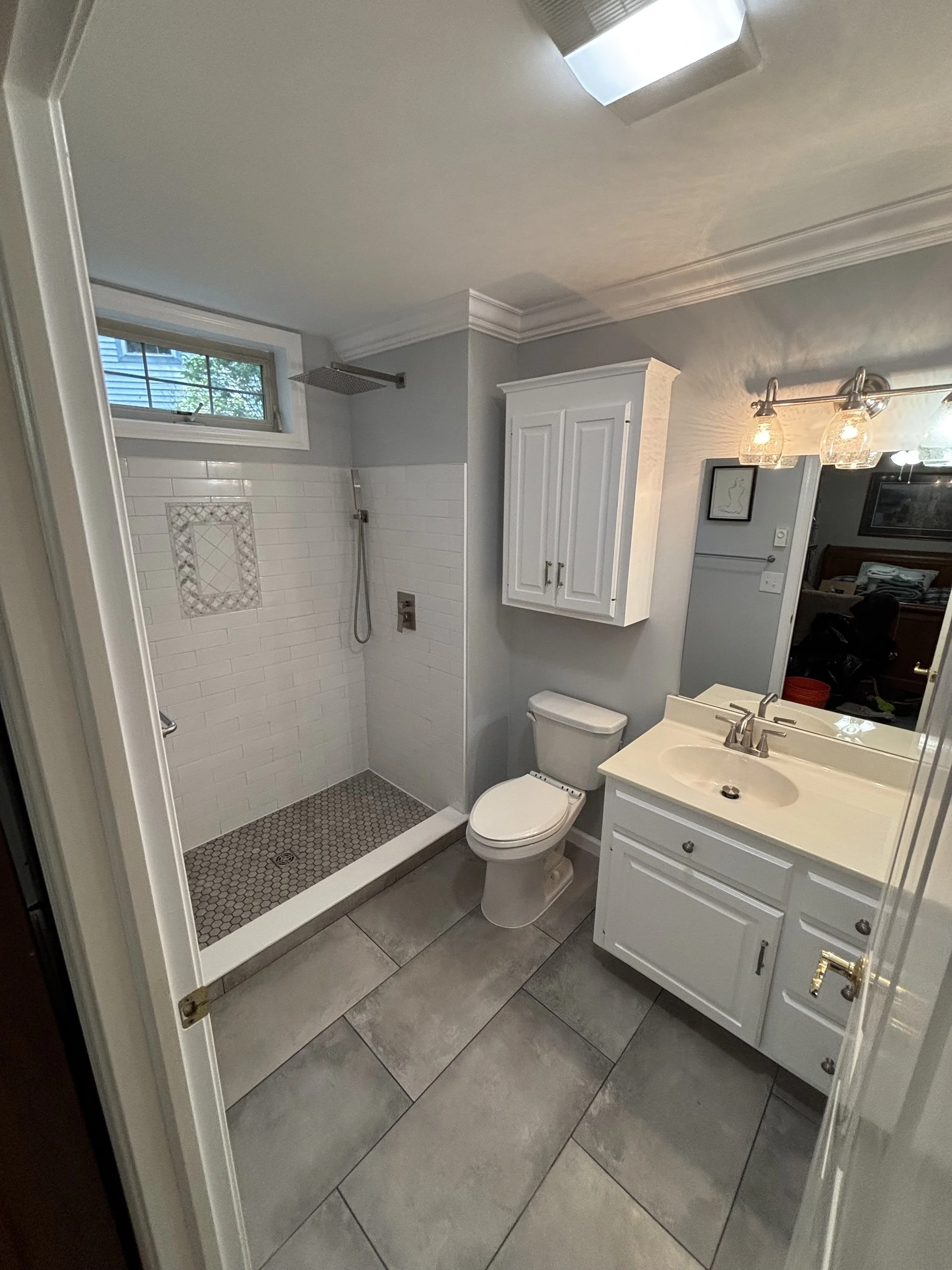 Bathroom renovation with tiled shower, vanity, toilet, and updated fixtures.