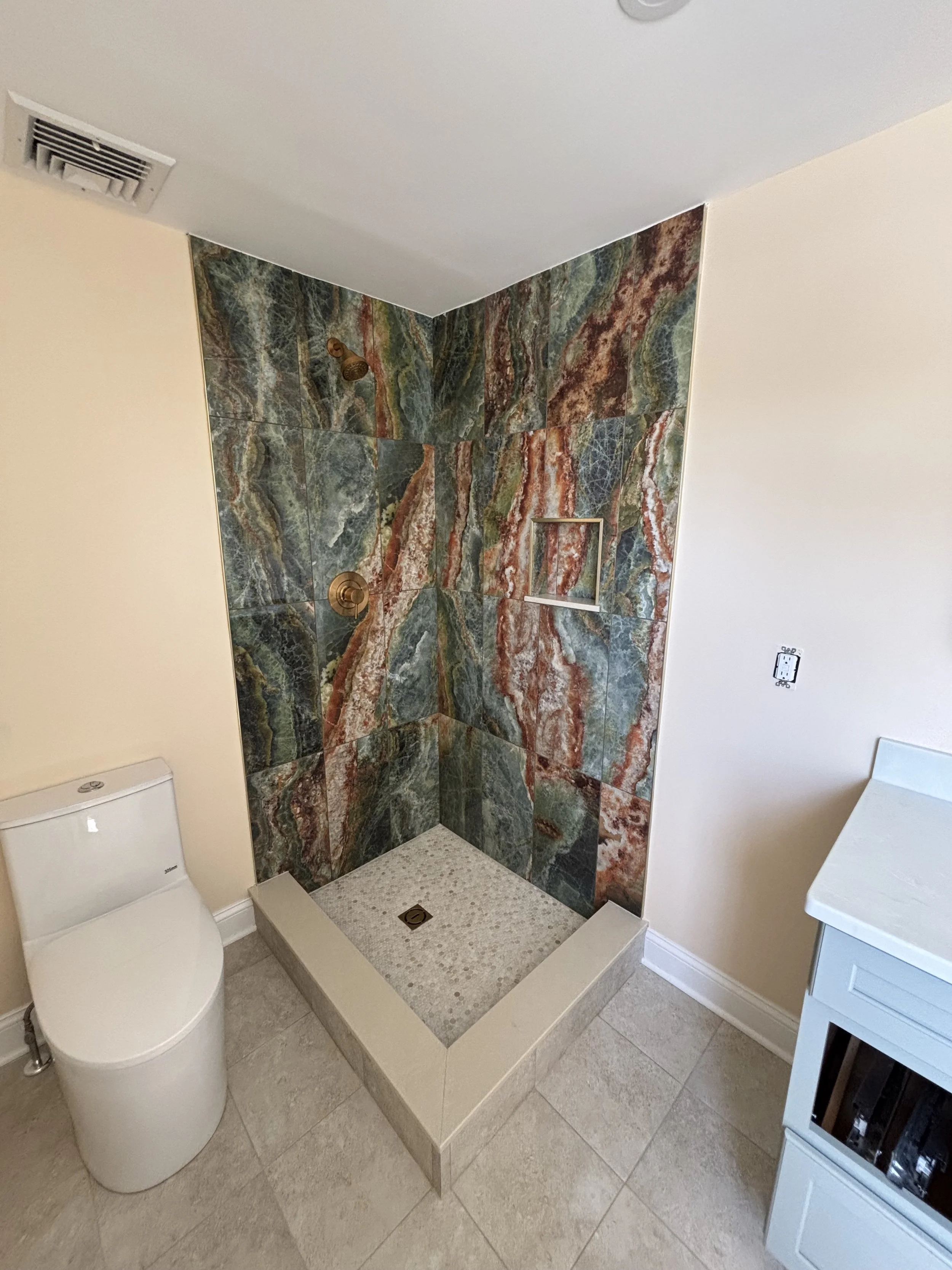 Bathroom renovation featuring tile shower with glass enclosure, vanity, toilet, and tile flooring.