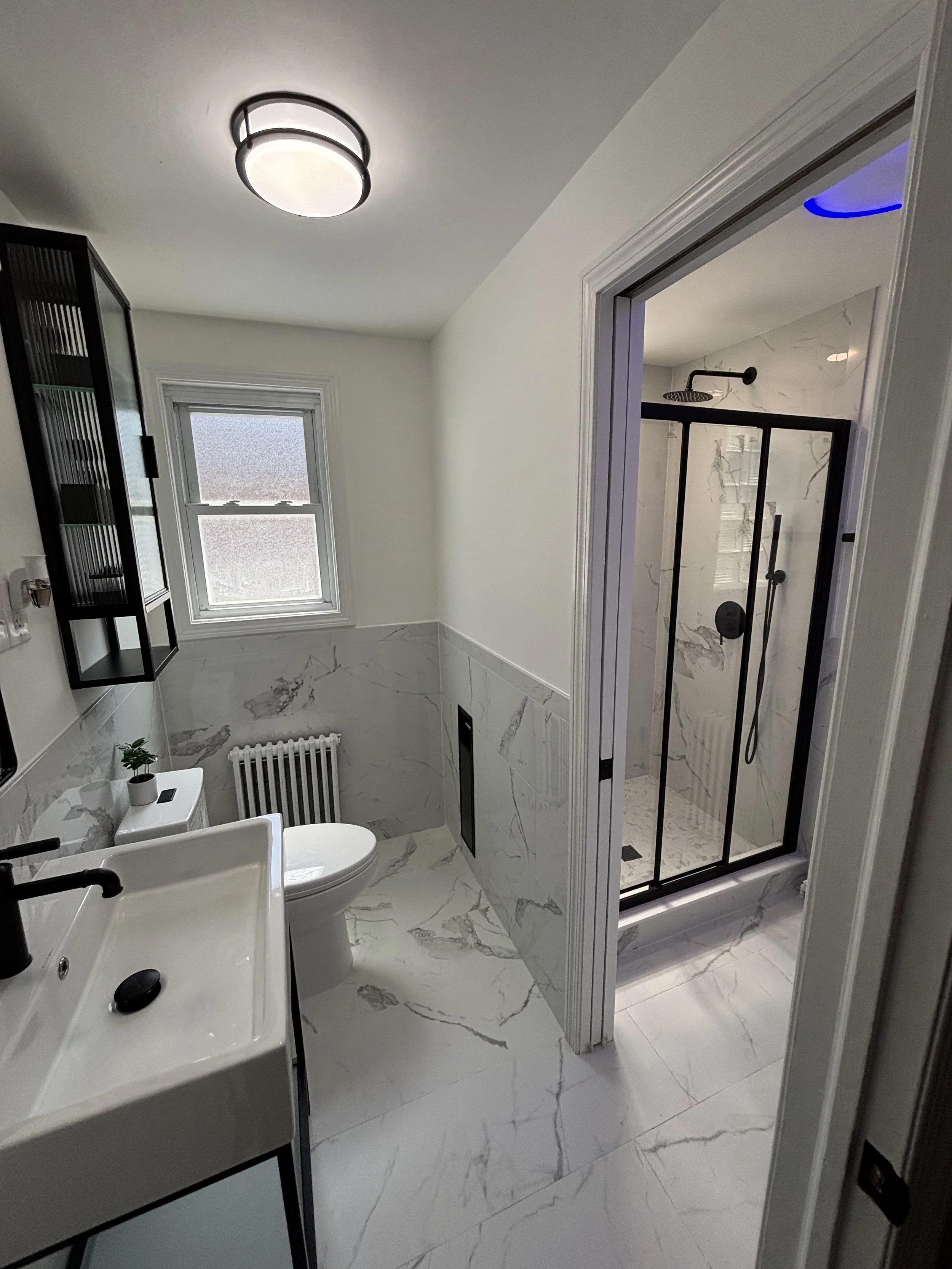 Bathroom renovation featuring marble-look tile shower walls and glass shower enclosure.