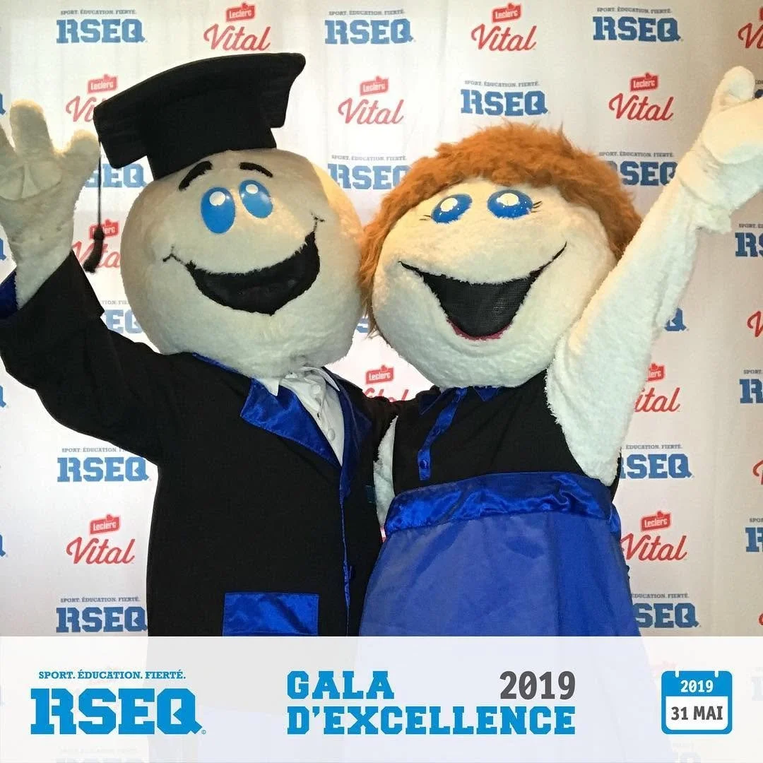 Deux mascottes en costume souriantes avec les bras levés, portant des costumes bleu et noir, lors d'une cérémonie de gala en 2019.