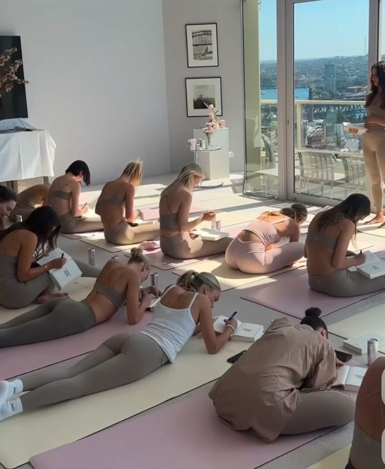 A group of women participating in a yoga or meditation class on mats near large windows with city view, under natural sunlight.