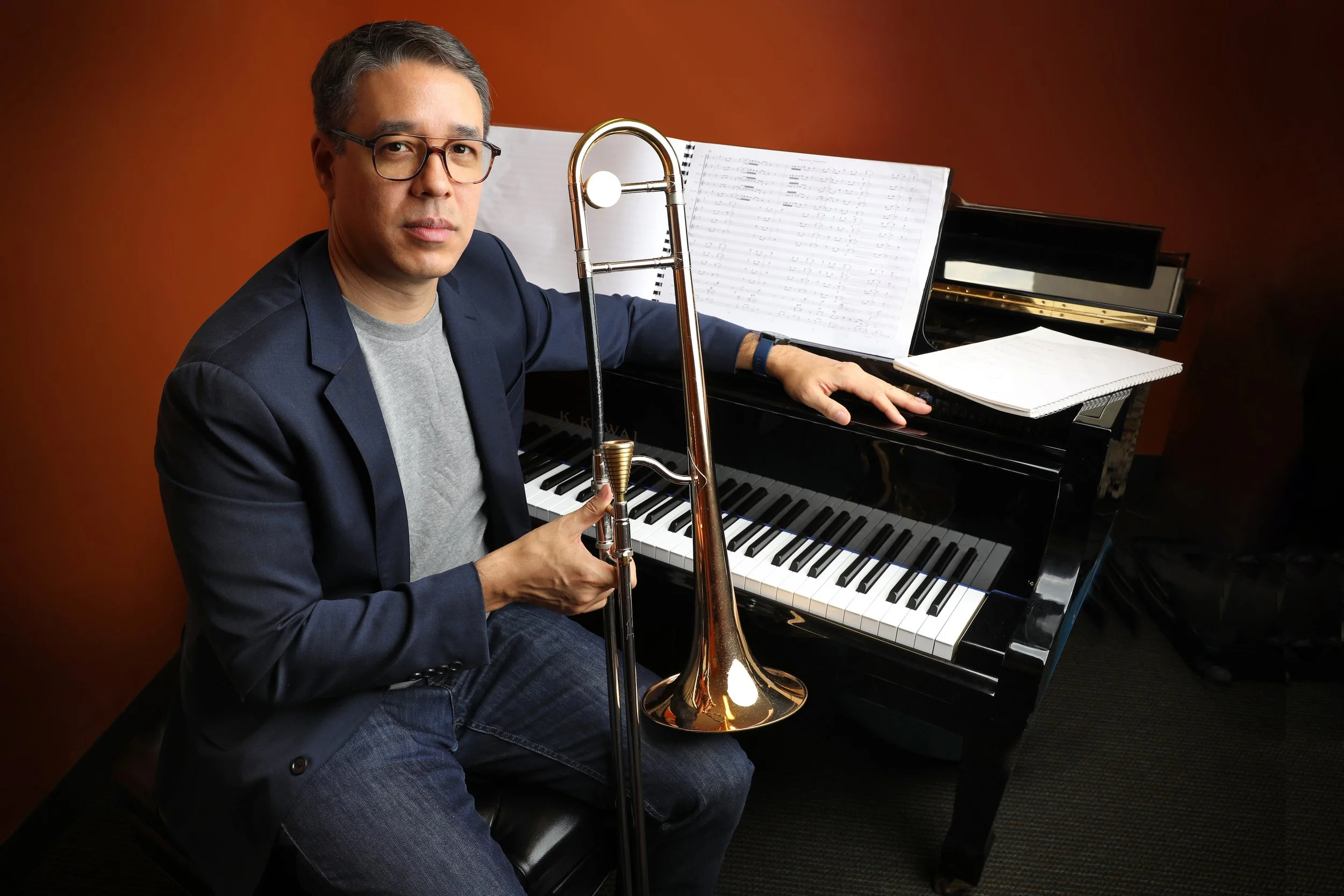 Trombonist John Yao sitting at a grand piano with sheet music