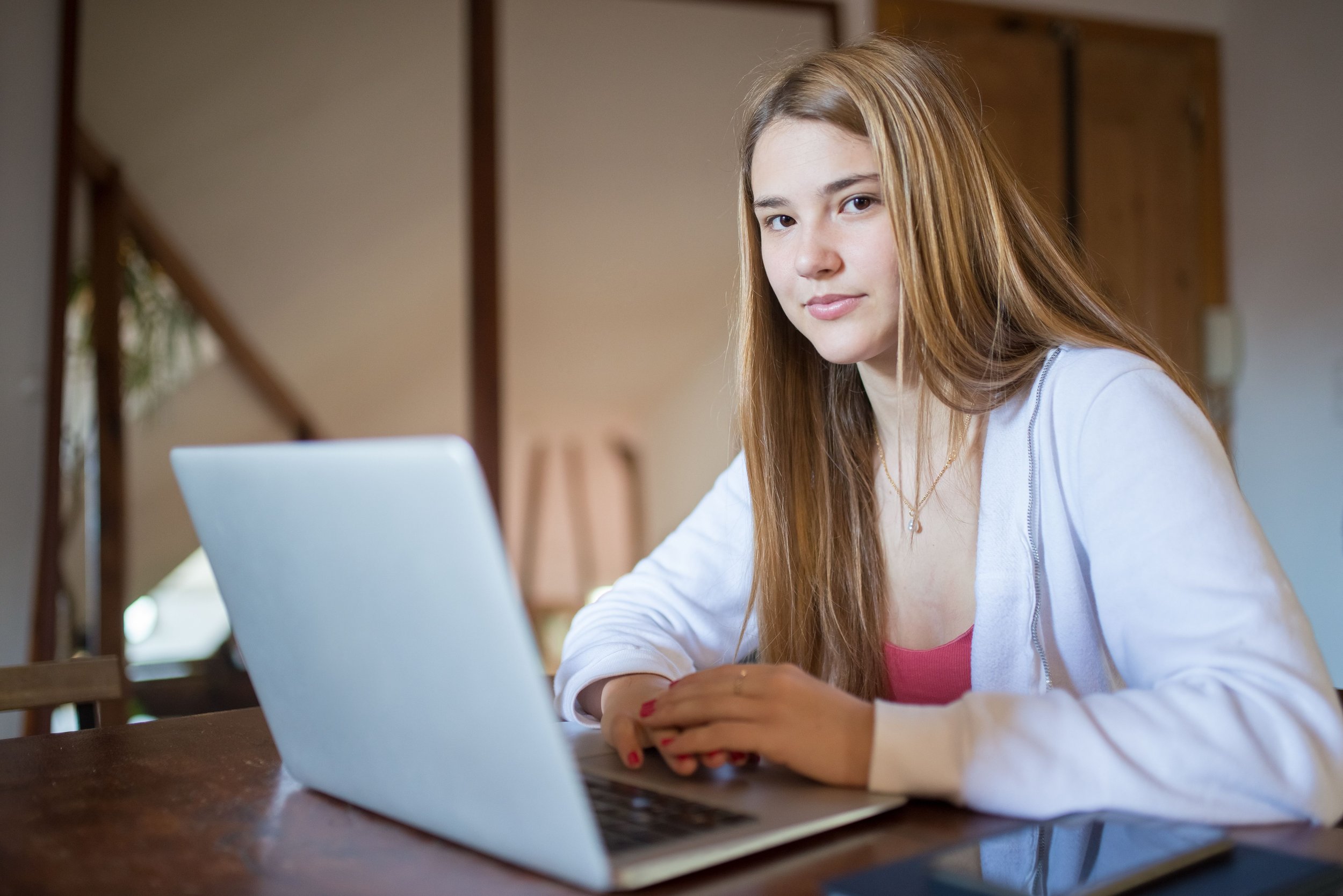 Young woman focused on a laptop at a wooden table in a cozy room.