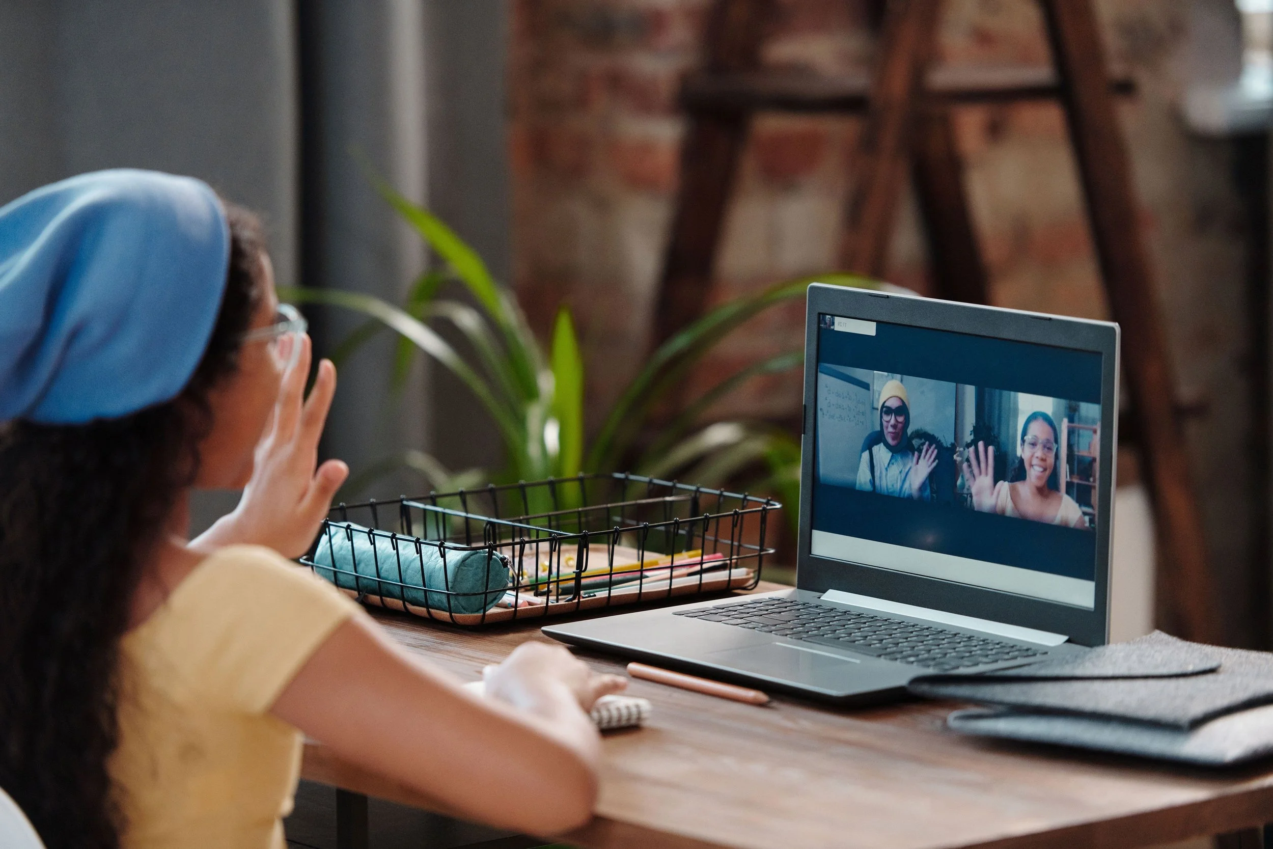 Teen student waving to two classmates on a laptop screen during a friendly online course.