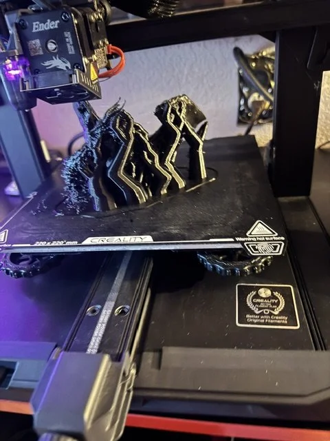 3D printer creating black and yellow filament sculptures on a print bed.