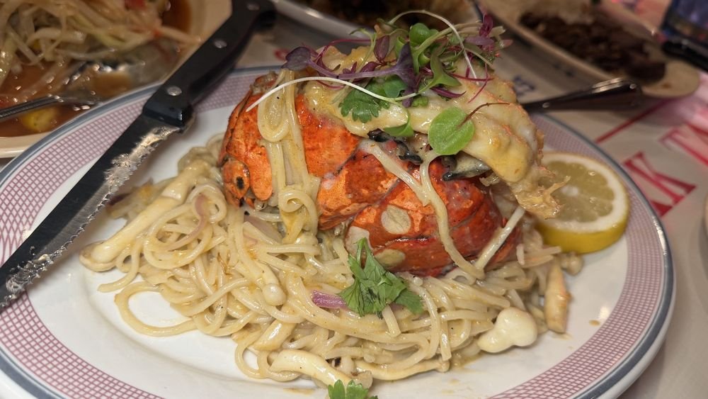 Lobster served over pasta, garnished with microgreens and lemon wedge.