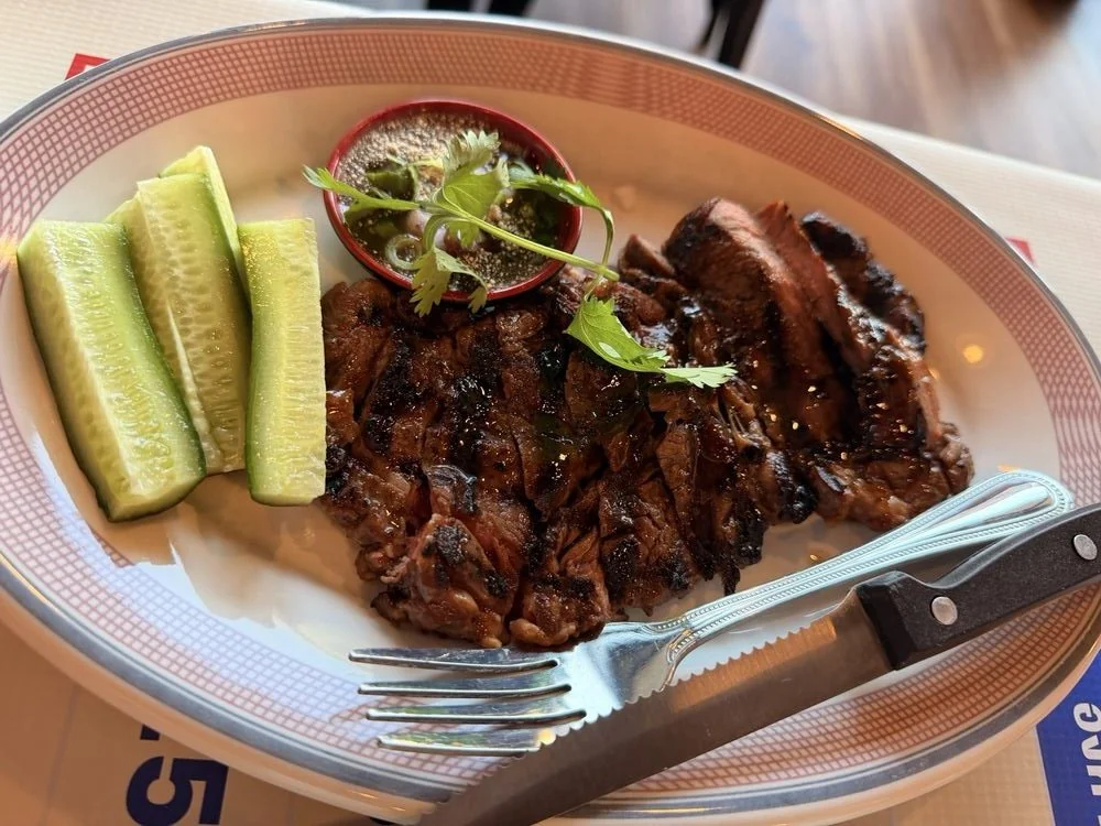 Barbecue ribs with sliced cucumbers and a small dish of sauce topped with cilantro on a white oval plate.