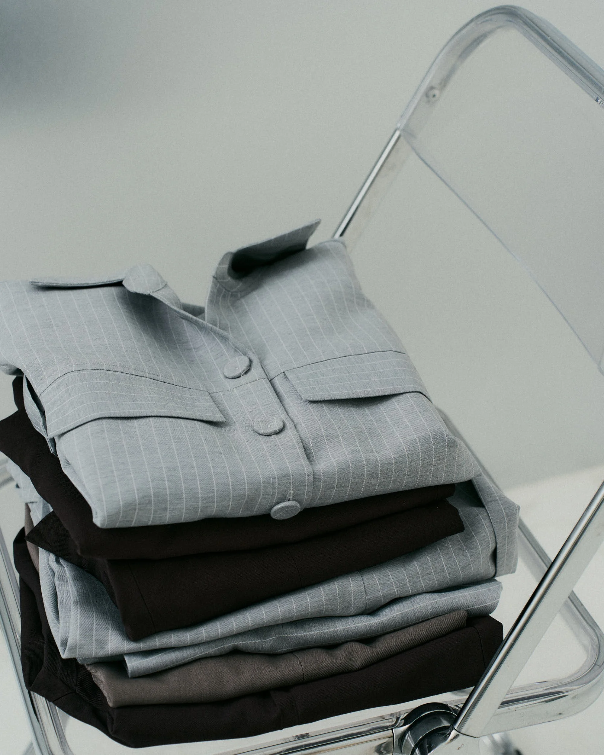 Pilhas de roupas masculinas em tons de cinza e preto organizadas em uma escada de metal com rodízios.
