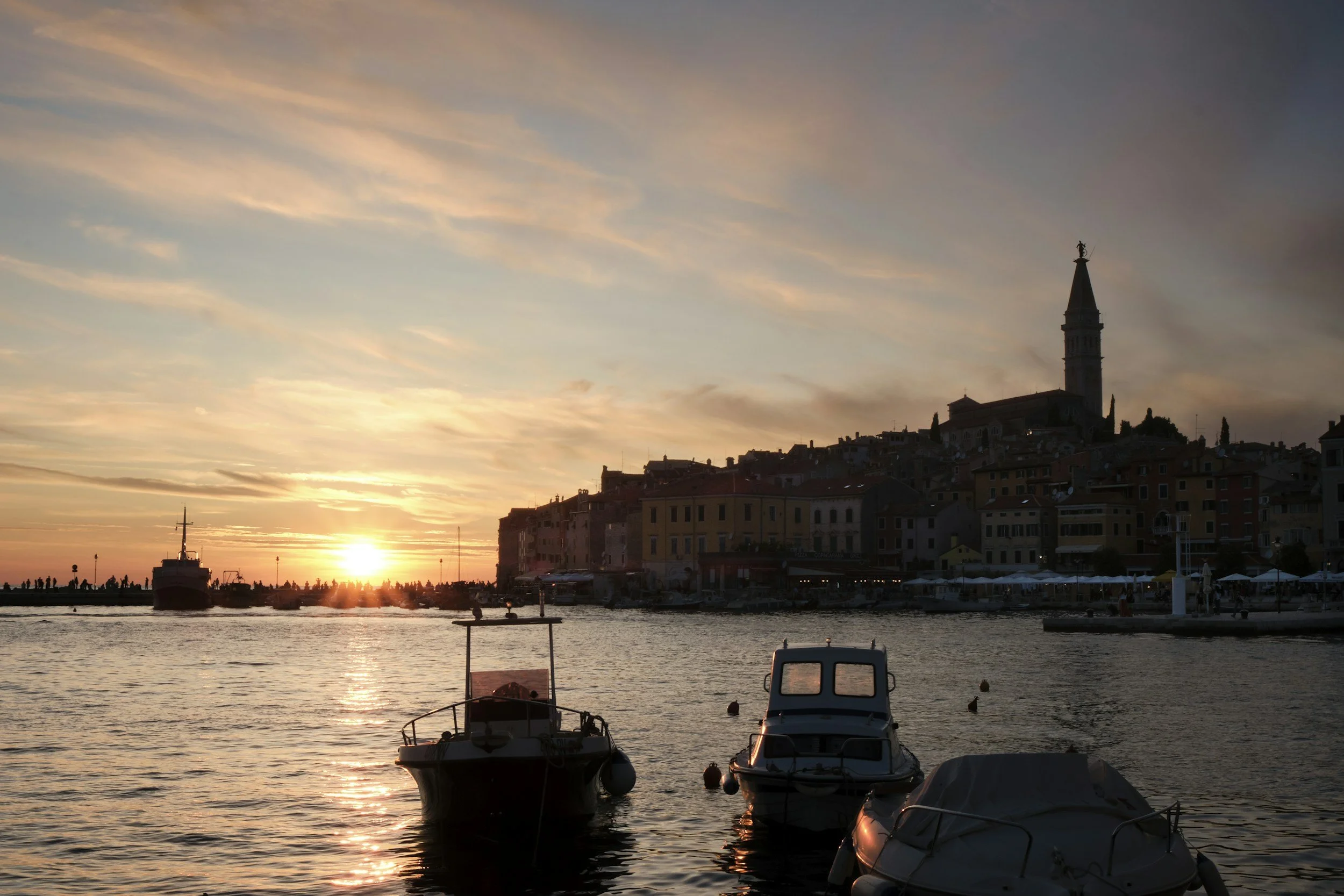 Boats in a Croatian harbor at sunset beside a hillside town.