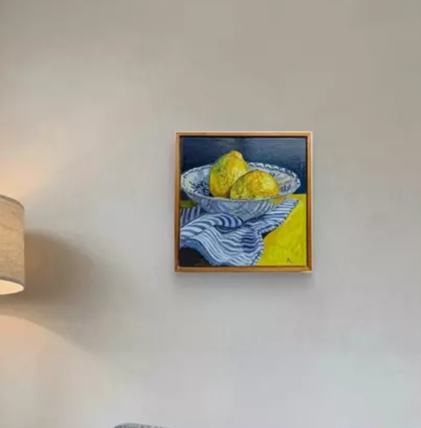 Painting of lemons in a blue and white bowl on a striped cloth, hanging on a light neutral  wall