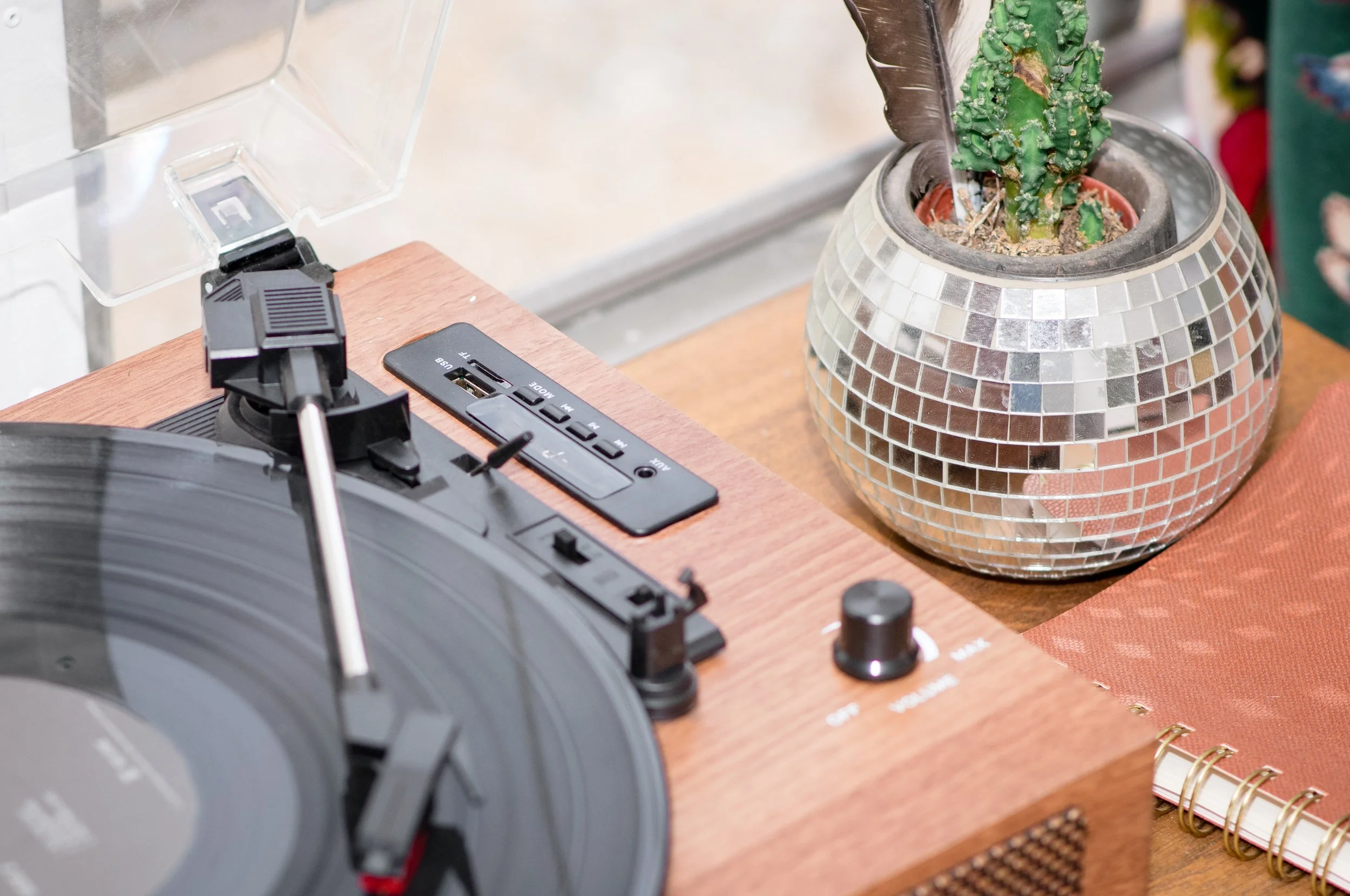 A turntable on a wooden surface next to a pot with a cactus plant decorated with mirror tiles.