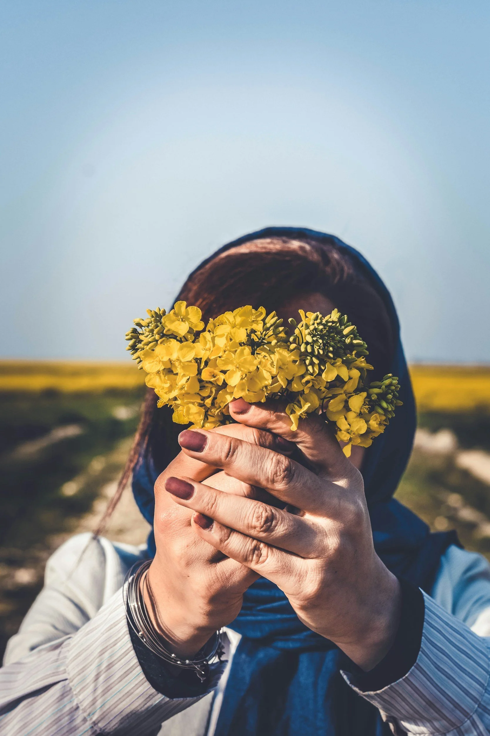 Person holding a bouquet of yellow flowers in front of their face, outdoors during daytime | Human Bean | Therapy Space for you to be Human