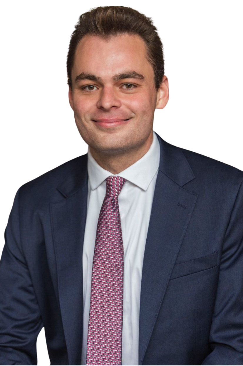 A man in a navy blue suit with a white shirt and a pink patterned tie, smiling and looking at the camera.