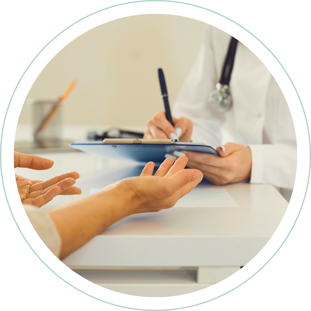 A healthcare professional, wearing a white coat and a stethoscope, taking notes on a clipboard while talking to a patient in a medical setting.