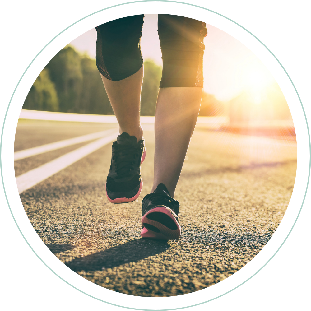 Close-up of a person jogging or running on a road during sunrise or sunset, wearing black athletic shoes and black athletic shorts.