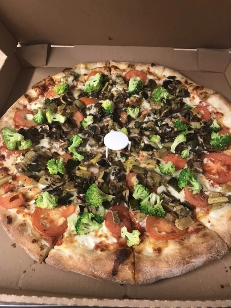 Vegetarian pizza with broccoli, tomatoes, black olives, and green peppers in a pizza box.