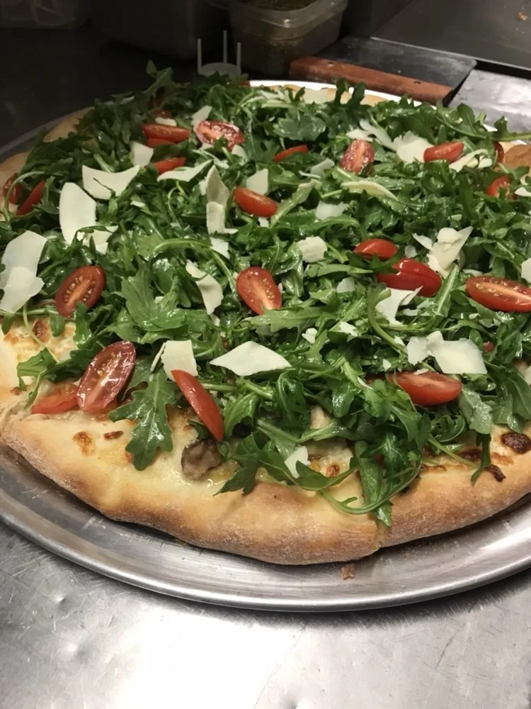 Fresh pizza topped with arugula, cherry tomatoes, and shaved cheese on a metal tray.