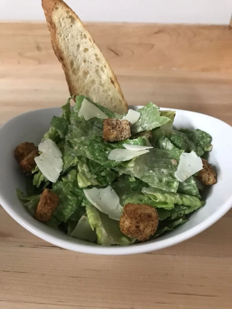 Bowl of Caesar salad with romaine lettuce, croutons, Parmesan cheese, and a slice of toasted baguette.
