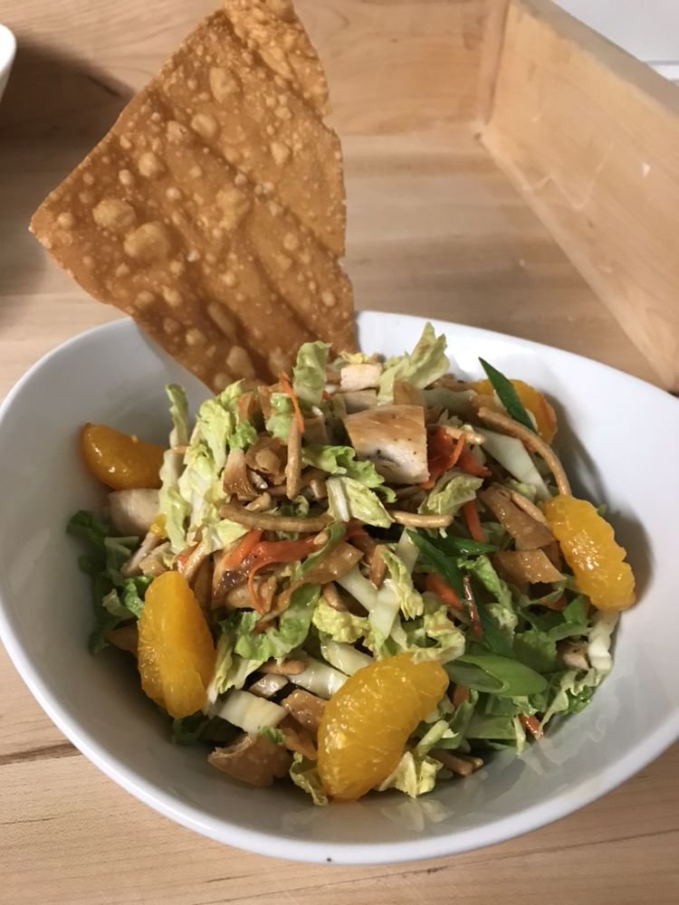 Bowl of salad with leafy greens, orange slices, shredded vegetables, and a crispy cracker on top.