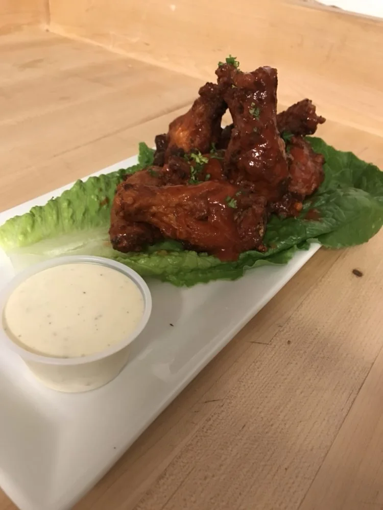 Plate of buffalo chicken wings with lettuce and a side of creamy dipping sauce.