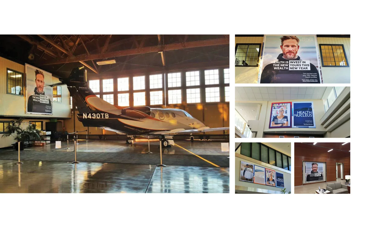 A private jet inside an aircraft hangar with large windows, surrounded by digital advertising screens displaying health and wealth messages.