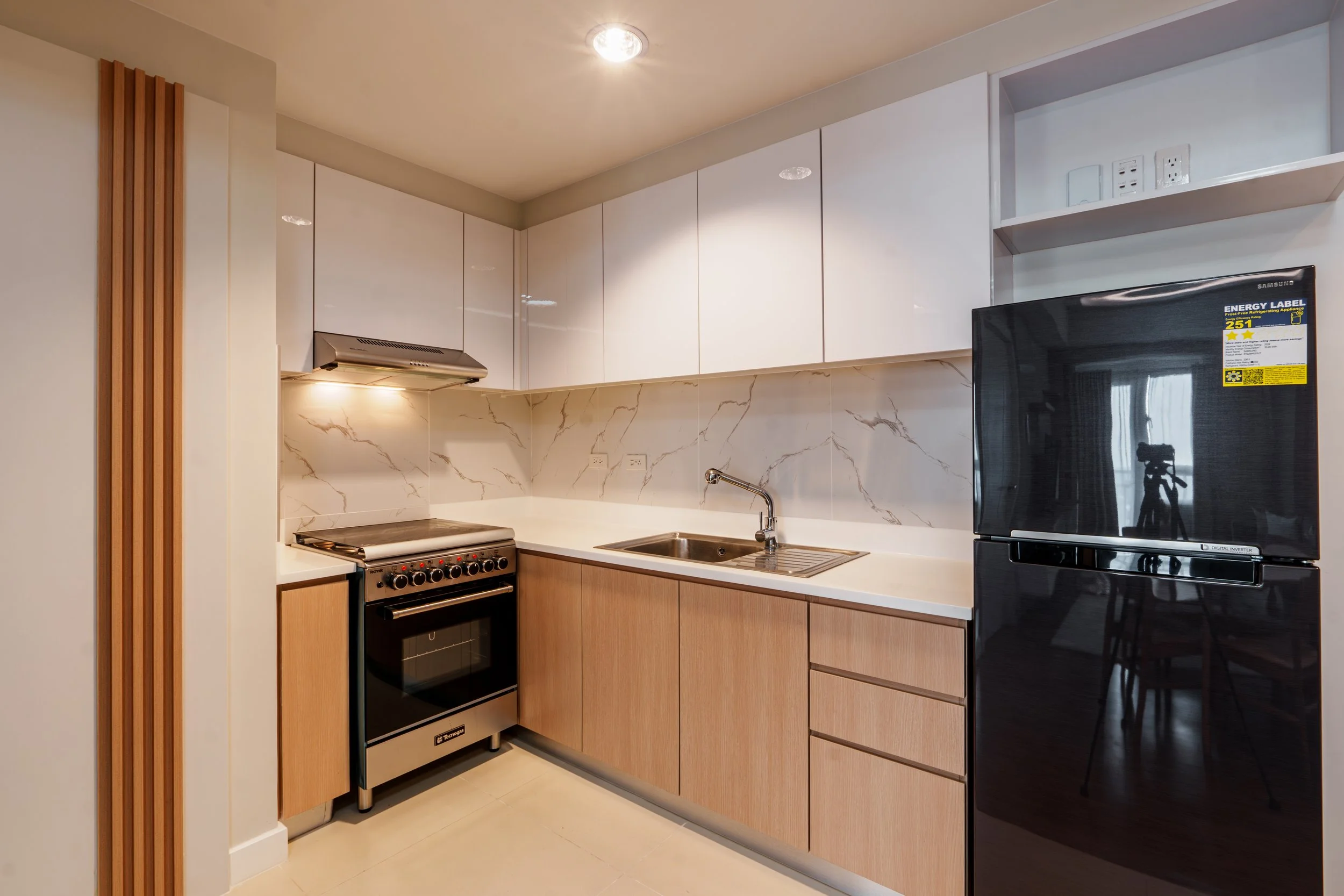 Modern kitchen with white cabinets, a marble backsplash, a black refrigerator, a stainless steel stove, and a small sink, with wooden panel accents on the left.