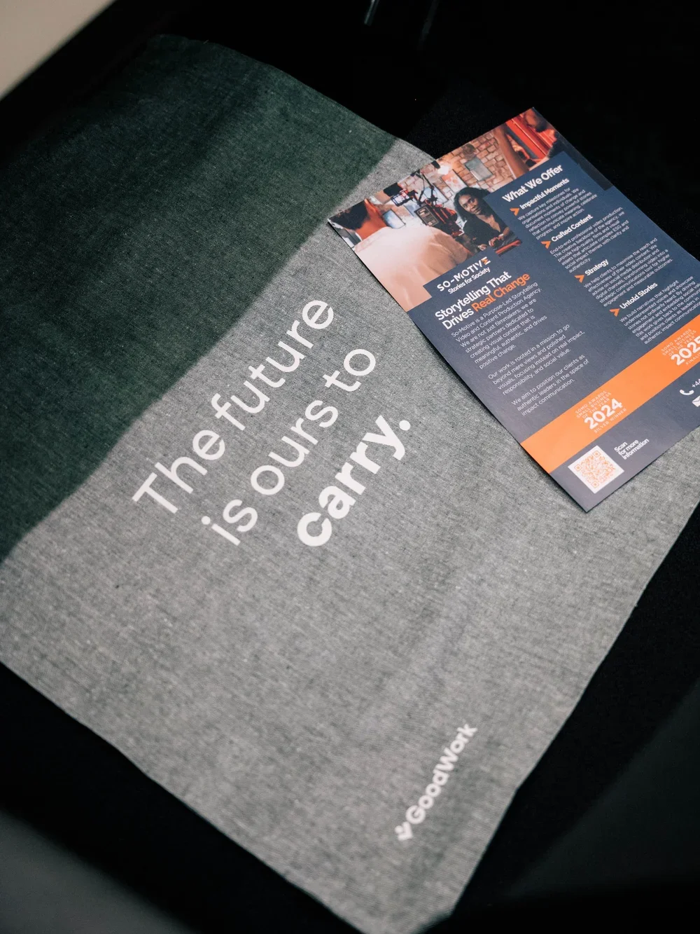 Photograph shows gray promotional booklet or bag featuring sustainability-focused slogan, “future is ours to carry,” beside colorful informational brochure.